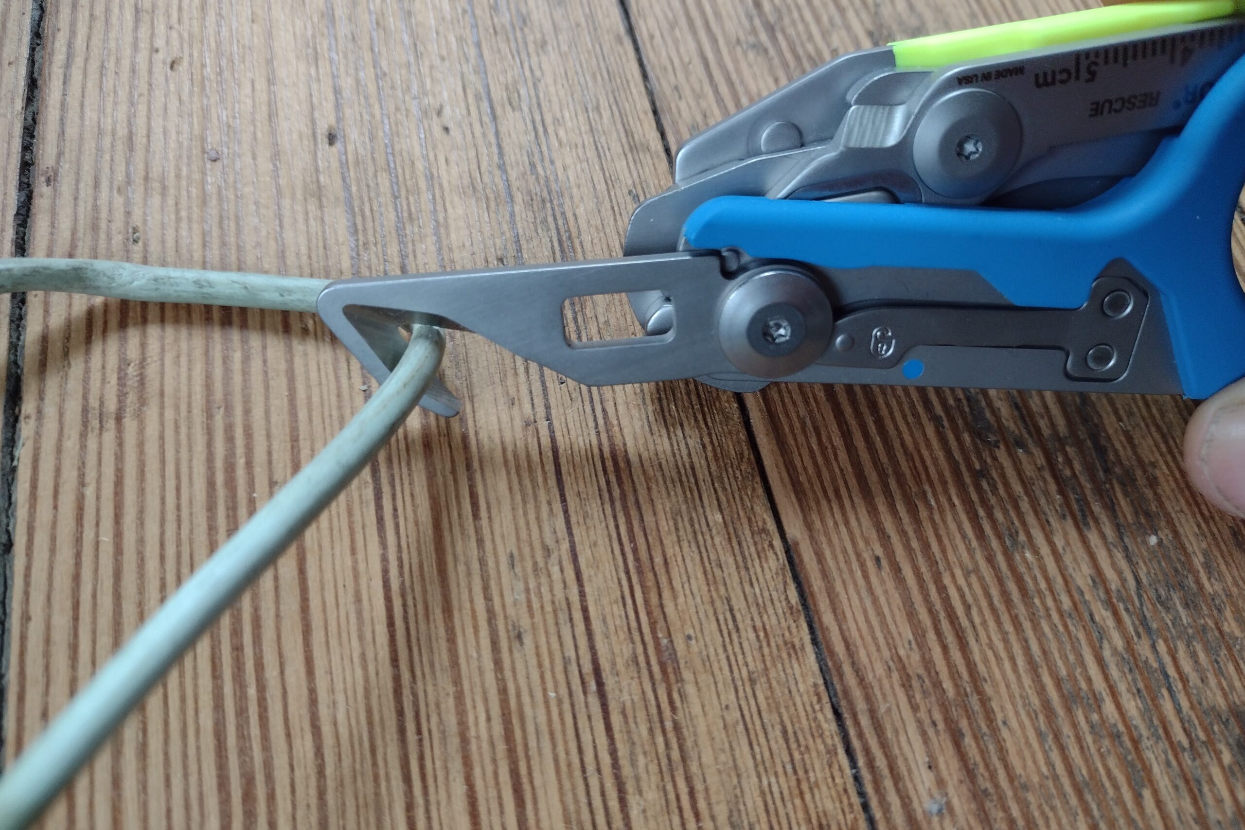 The Leatherman Raptor with its strap cutter extended, cutting an electrical wire.