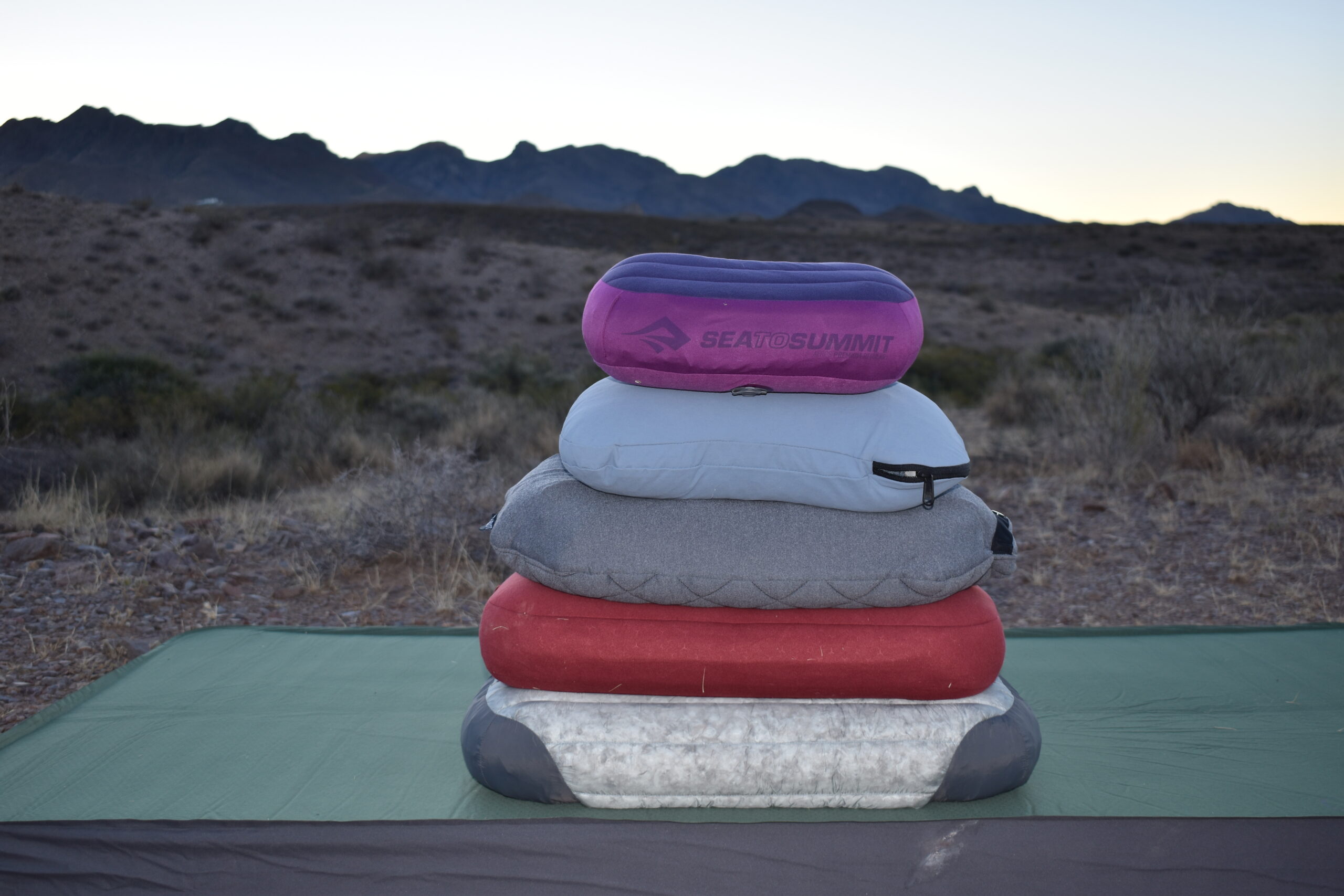 5 camping pillows stacked on a sleeping pad in the desert with mountains in the background