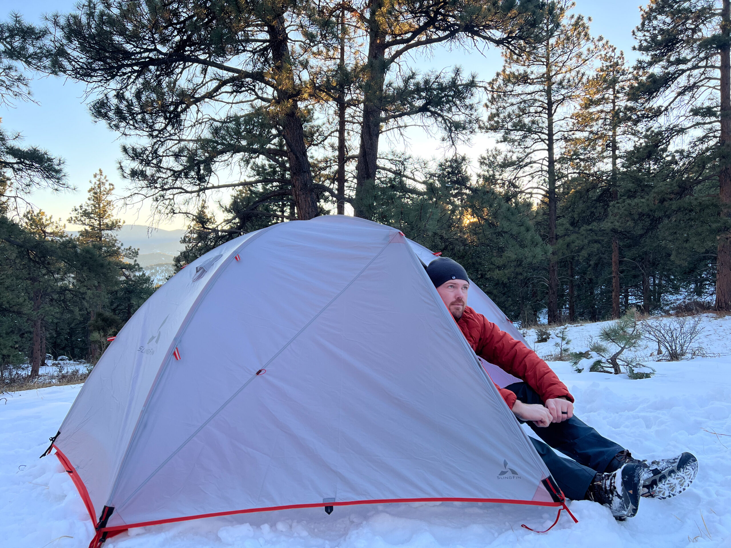 Person sitting at the entrance of the SlingFin CrossBow 2 tent in a snowy forest.