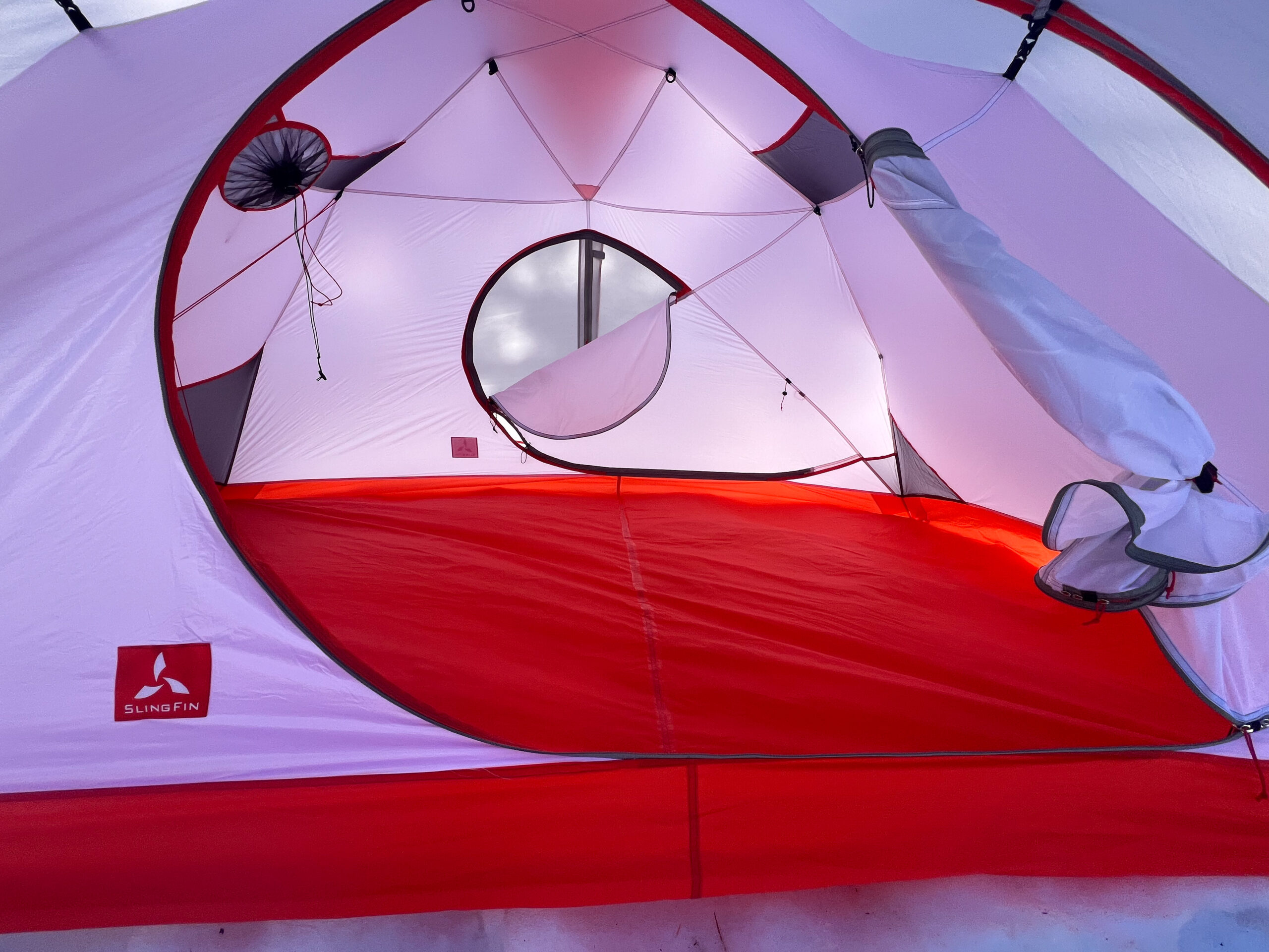 Interior view of the SlingFin CrossBow 2 tent with red flooring and white walls, featuring storage pockets and gear loops.