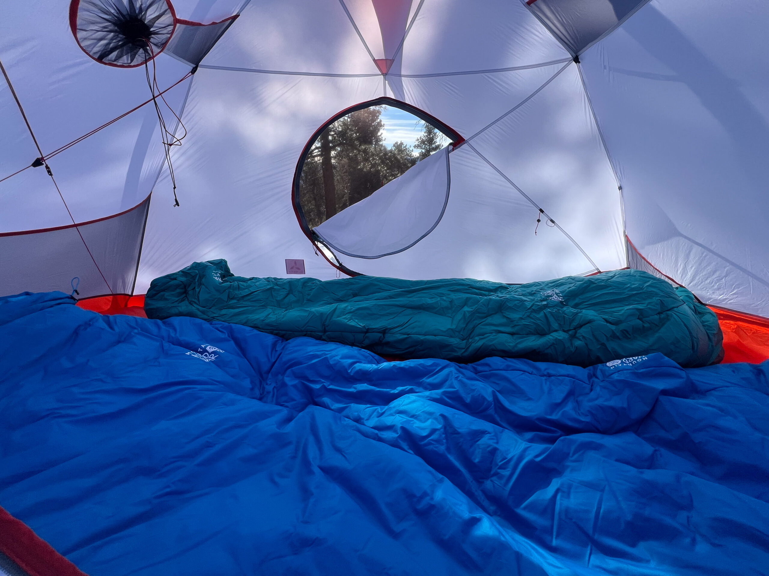 An interior image of a tents looking through an open door. There are trees outside and two sleeping bags in the for ground.