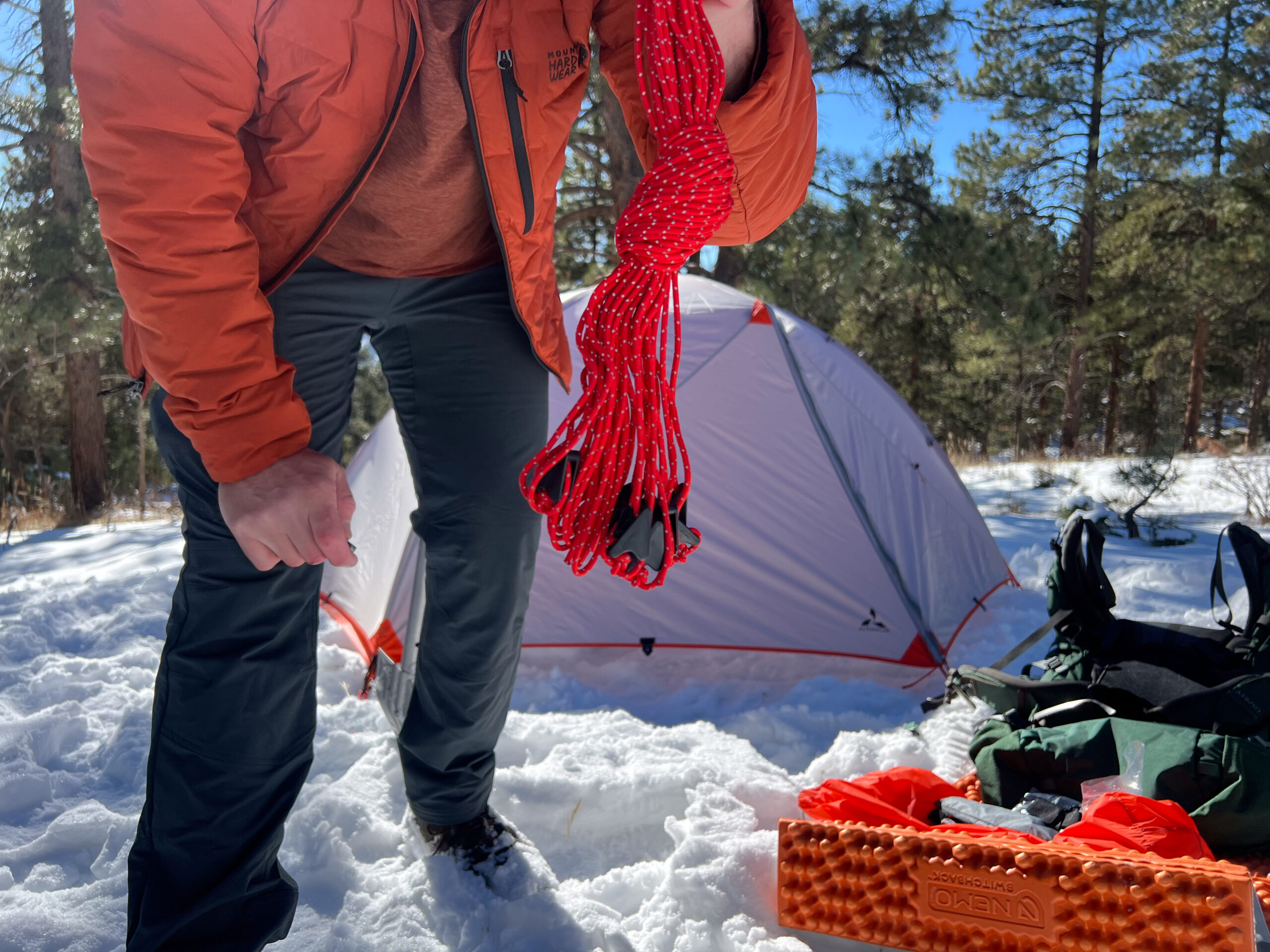 Close-up of a person holding red guy lines with the SlingFin CrossBow 2 tent in the background.