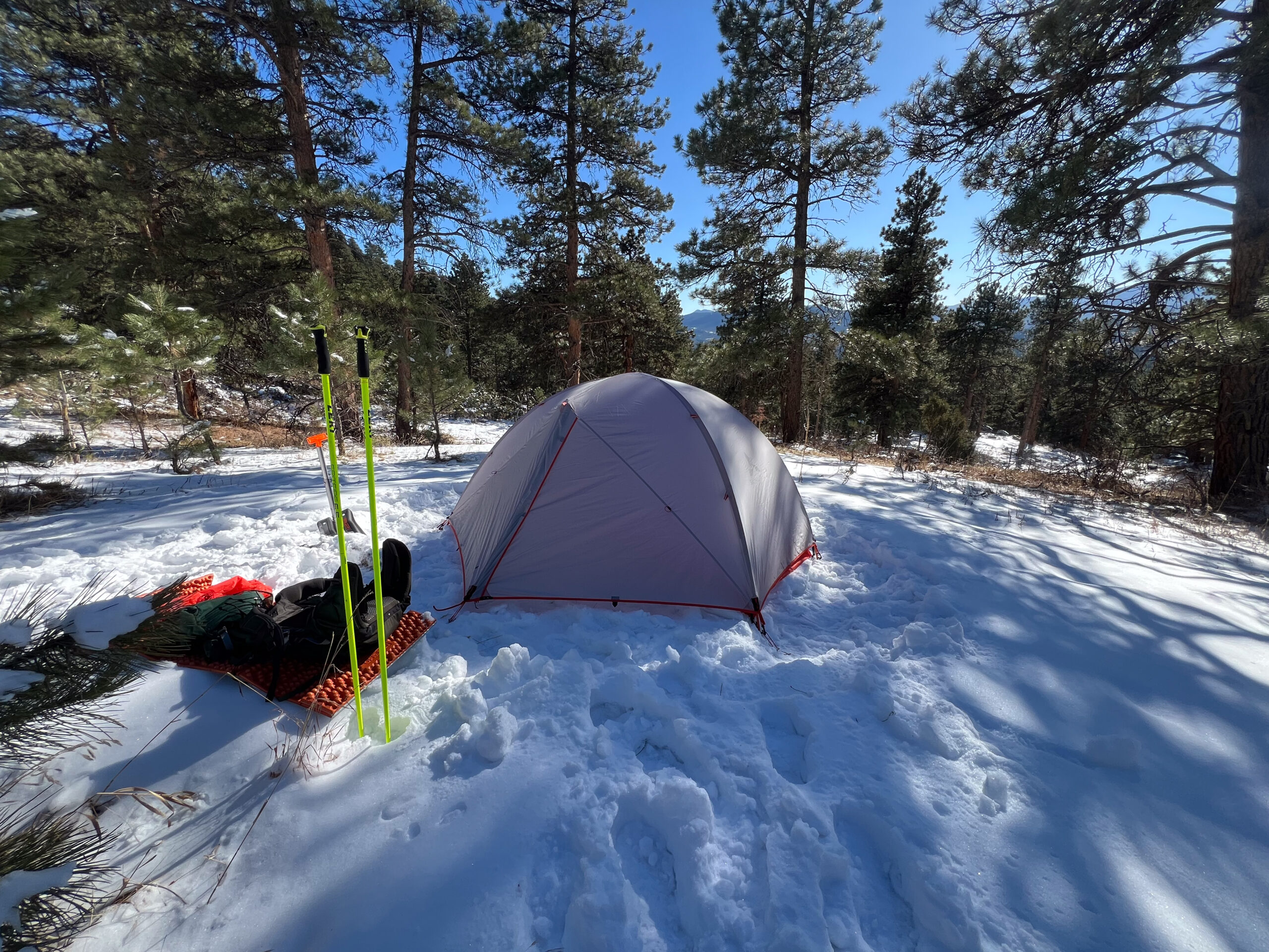 The SlingFin CrossBow 2 tent in a snowy forest with trekking poles and camping gear outside.