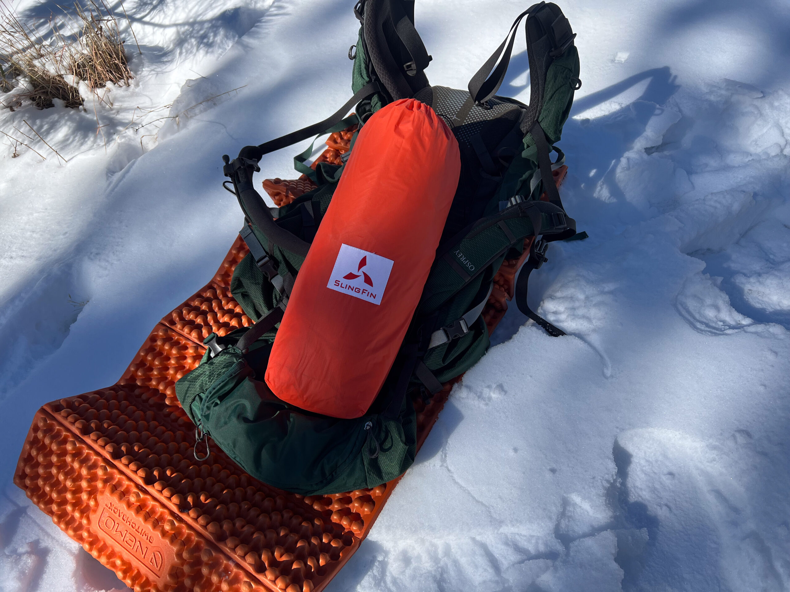 SlingFin CrossBow 2 tent packed in an orange storage sack on top of camping gear in the snow.