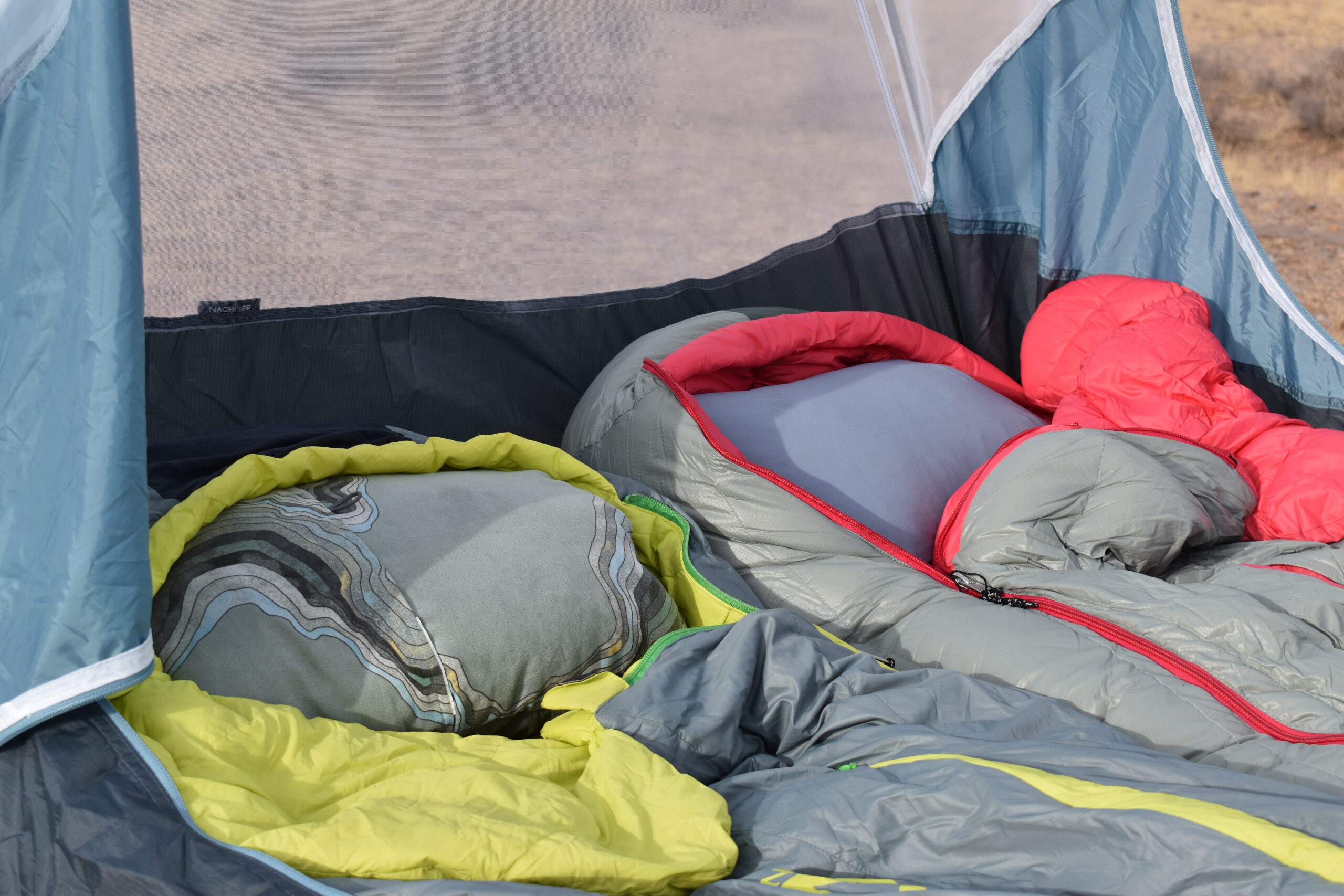 A close up of the Therm-a-rest Compressible pillow (left) and HEST Camp Pillow (right) side by side in the hoods of two mummy-style sleeping bags in a tent