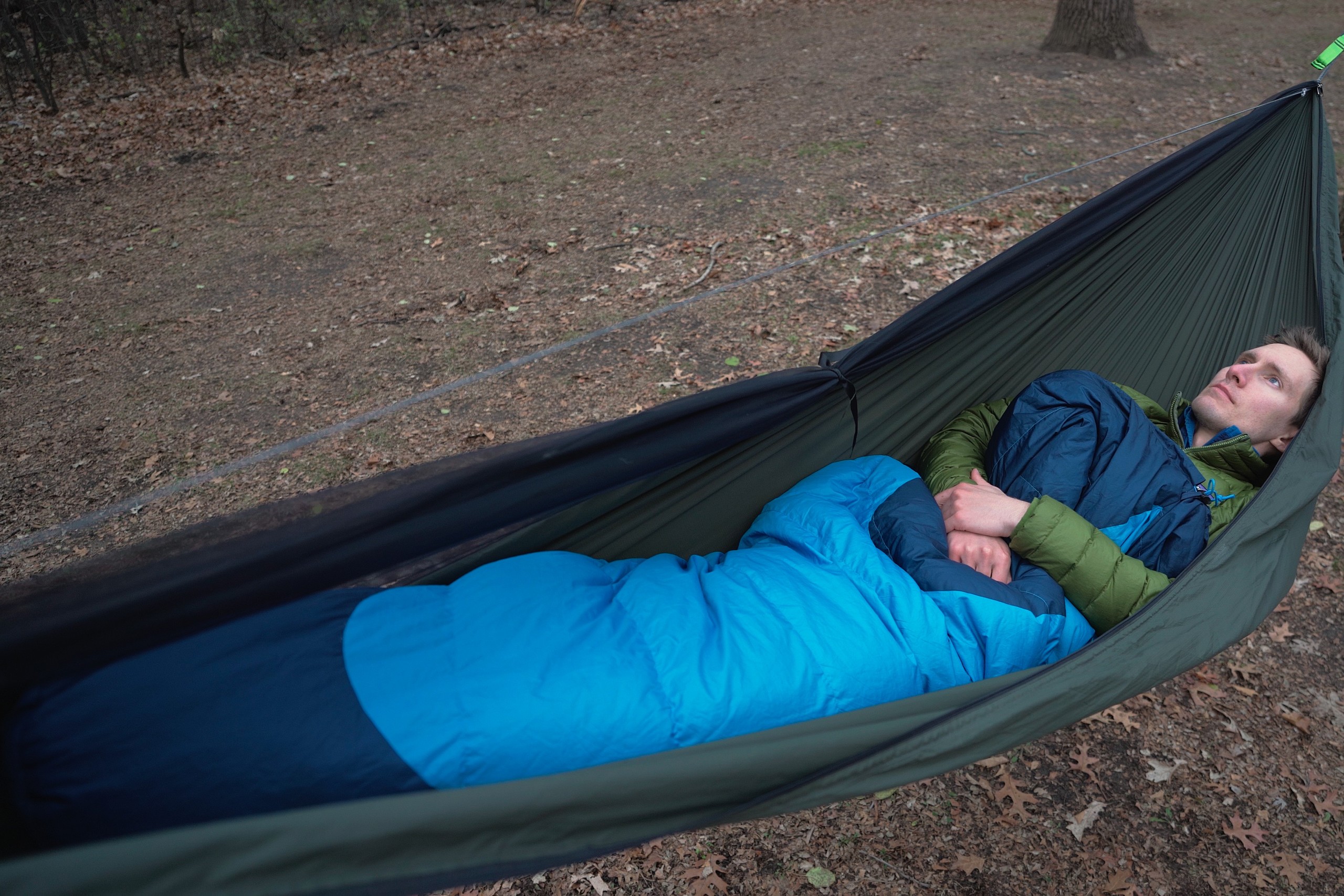 A man in a blue sleeping bag rests in a green hammock