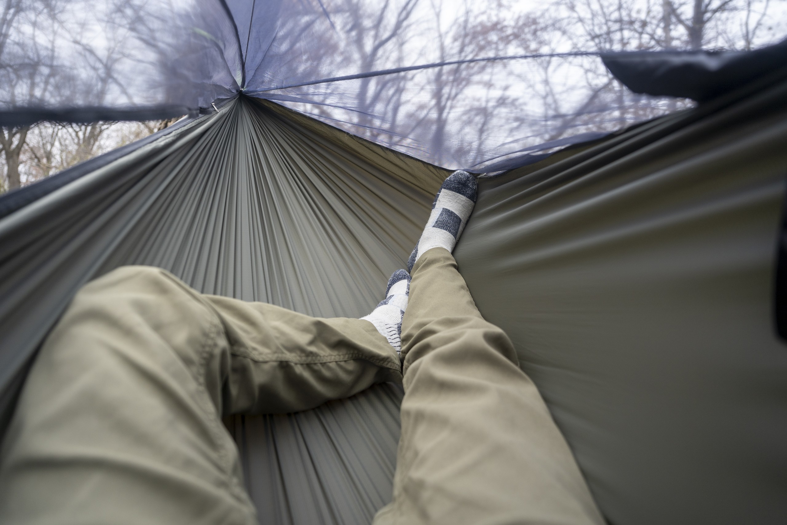 A pair of legs stretch into a green hammock from a point of view perspective