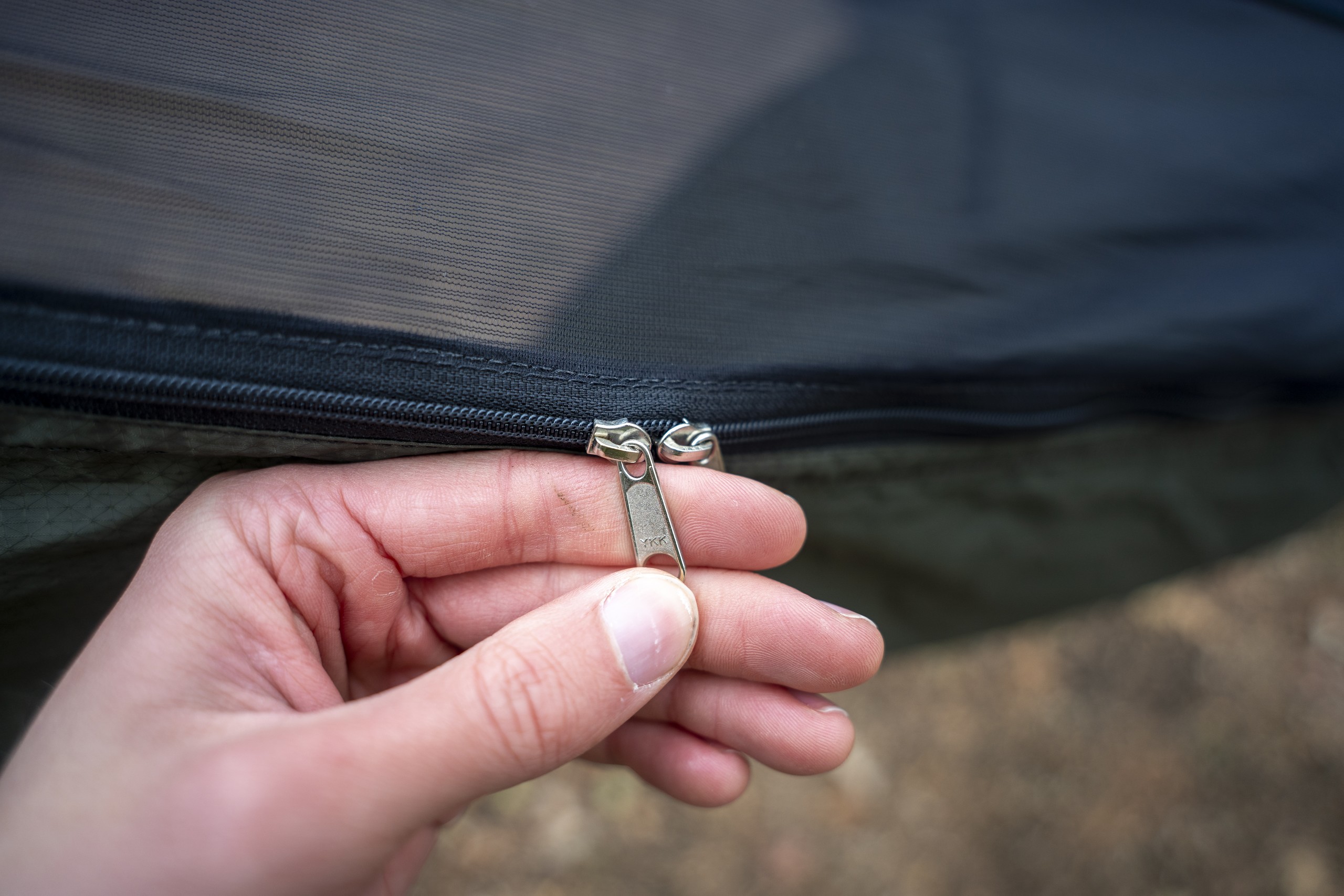 A hand holds zipper pulls on a hammock