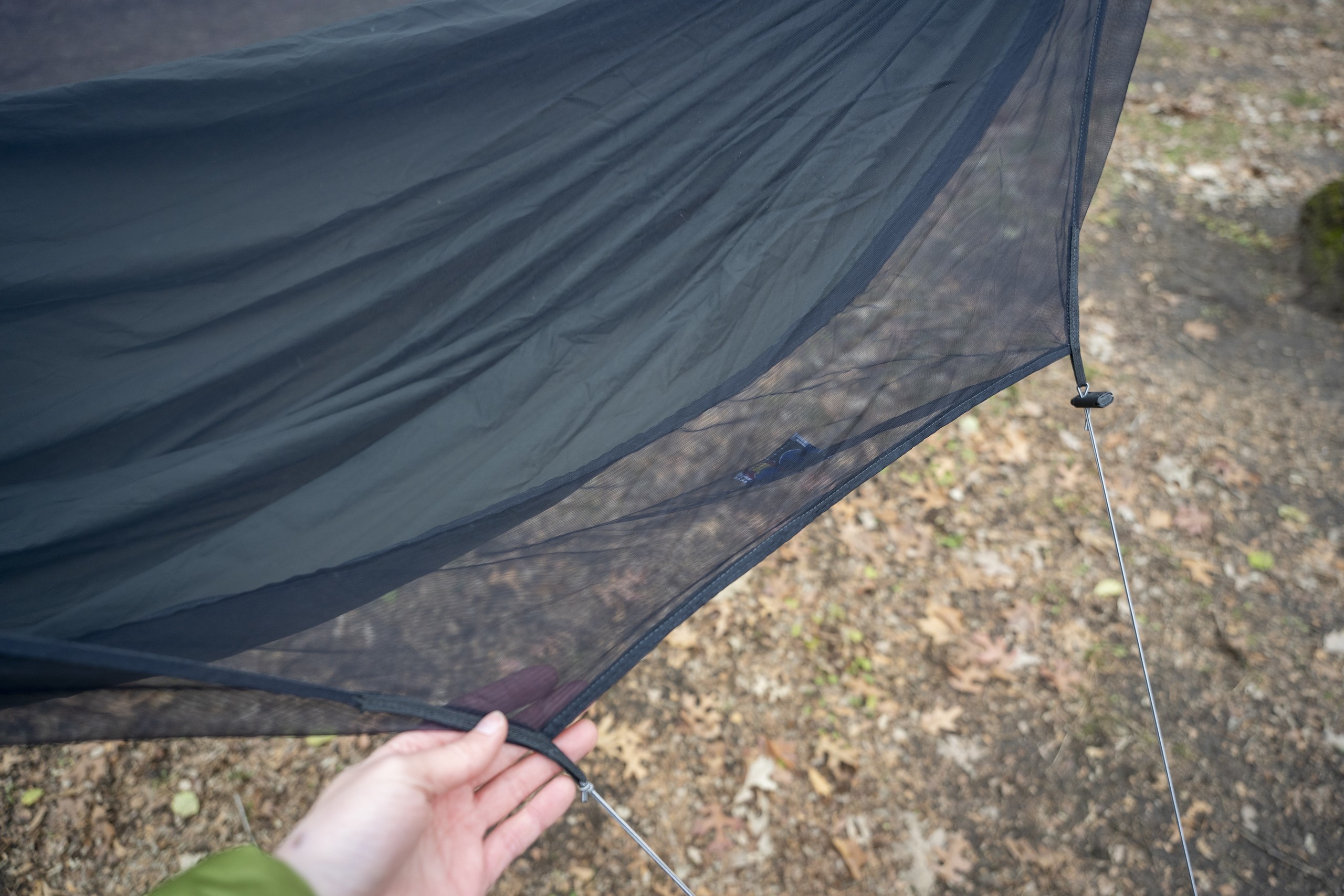 A hand holds the mesh of a netted hammock