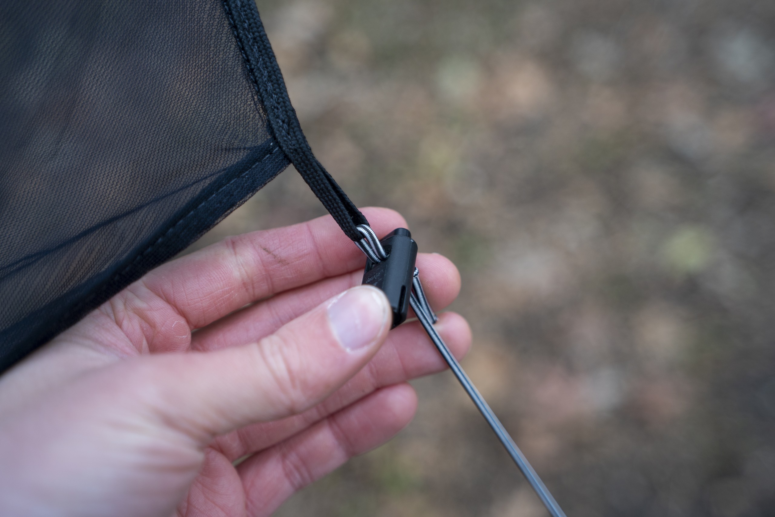 A hand holds a cord lock attached to mesh