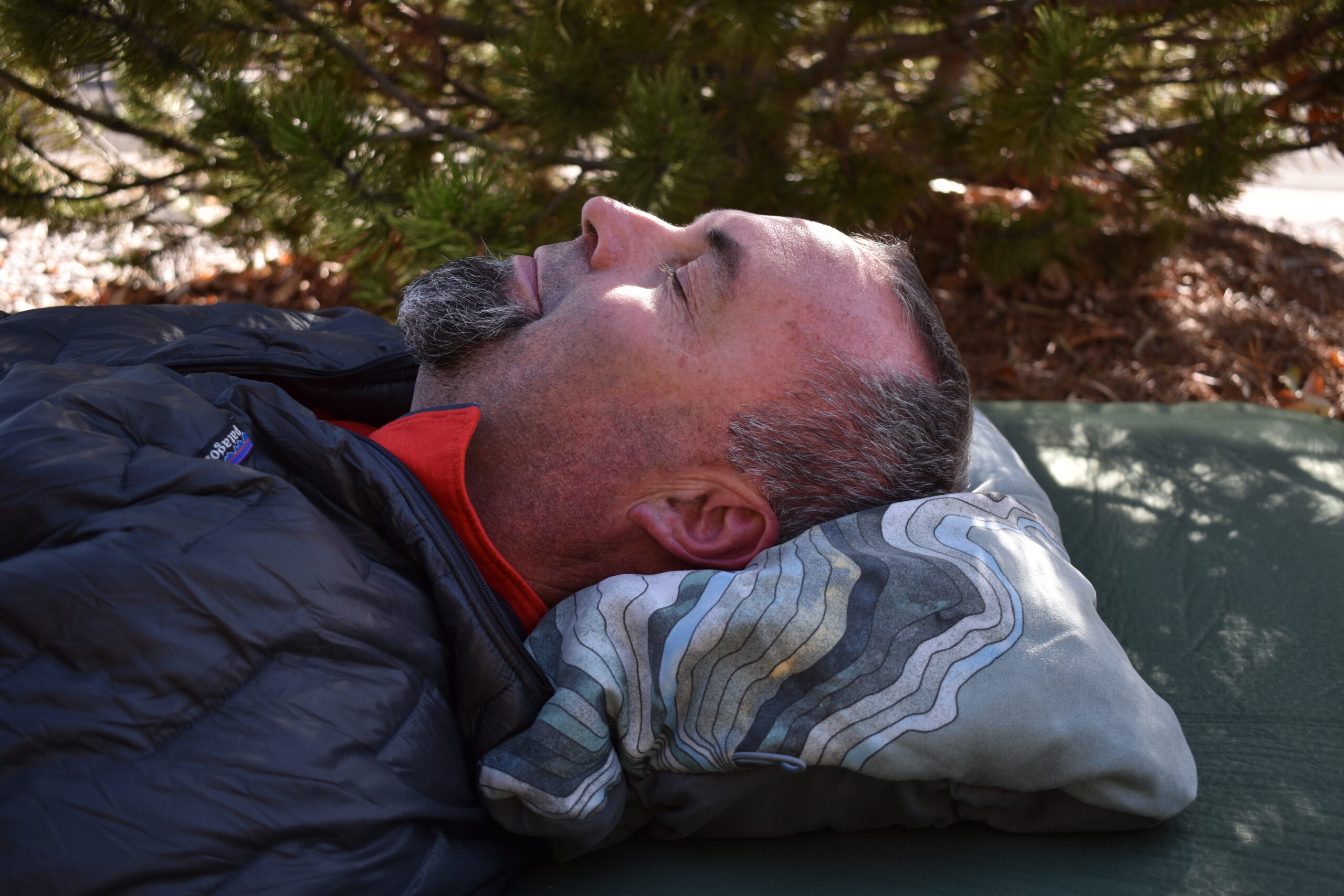 Close up of the author resting comfortably on the Therm-a-rest Compressible pillow in front of evergreens