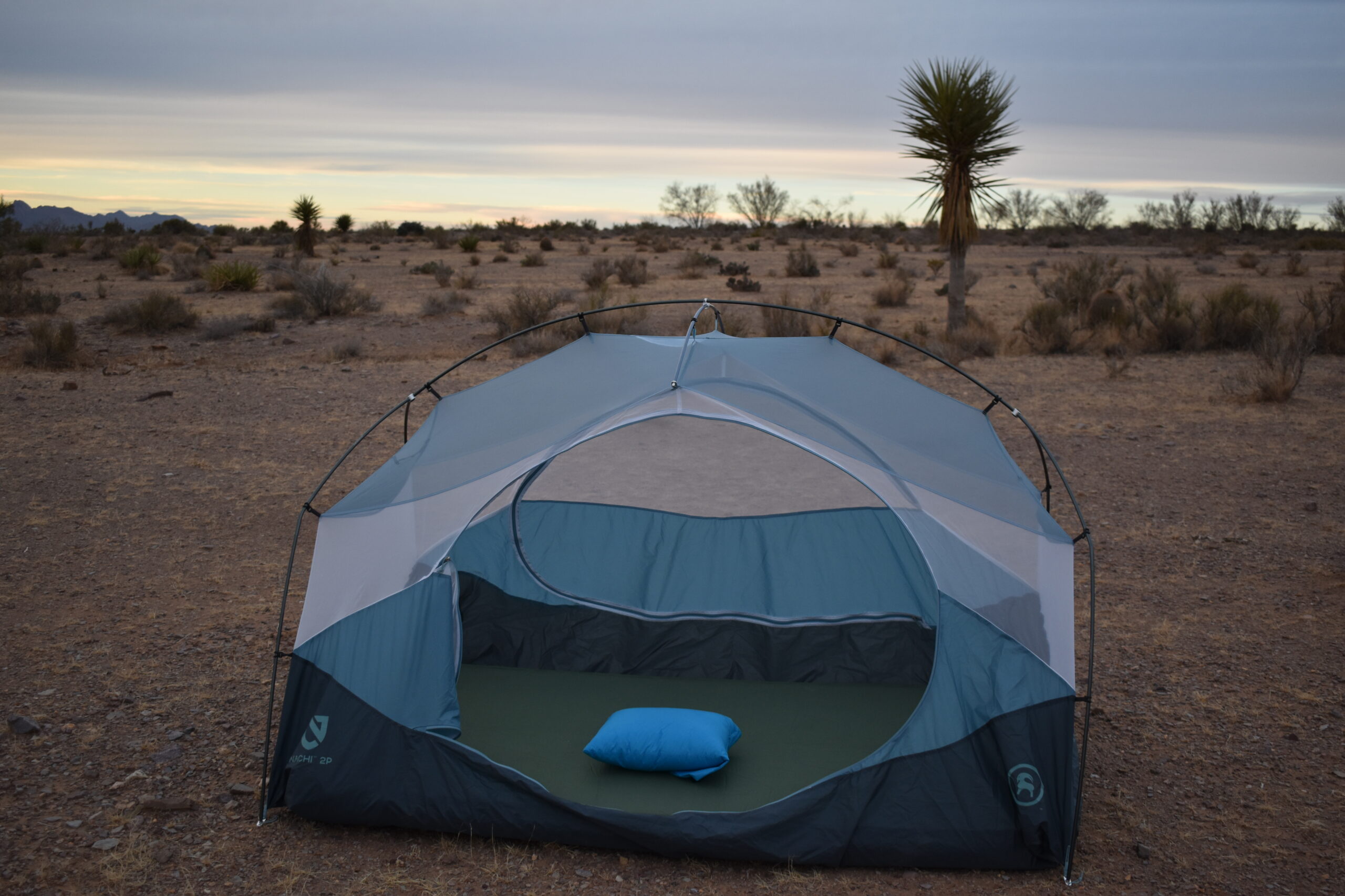 The Cloudrest Down Pillow is on a sleeping bad inside an open tent pitched in the desert near a Joshua Tree