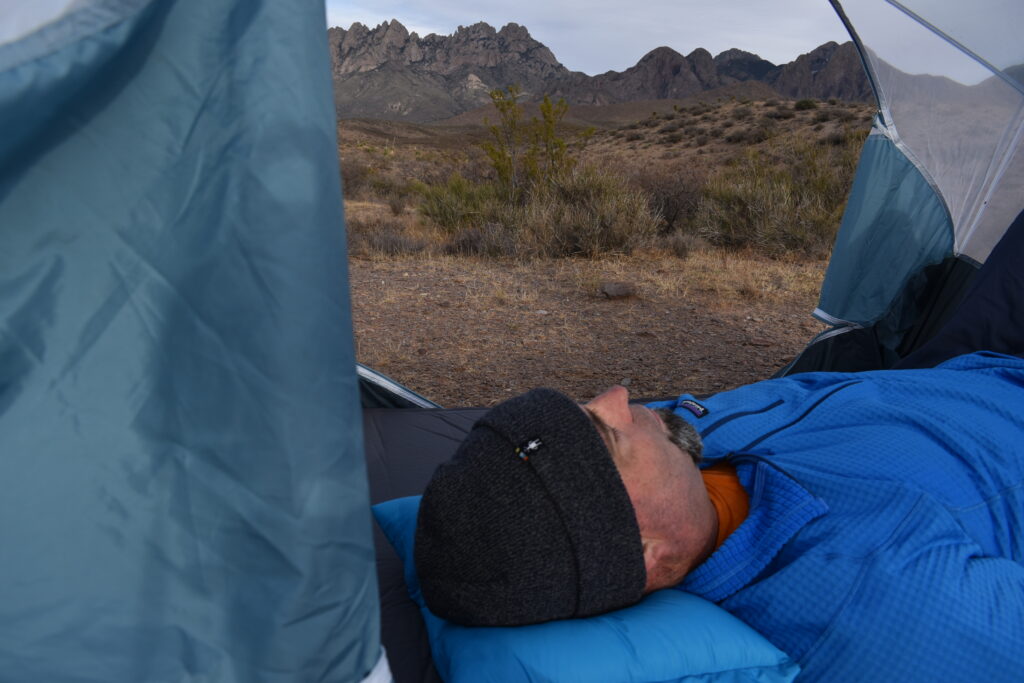 The author laying on the Western Mountaineering Cloudrest Pillow with the Organ Mountains visible behind his tent.