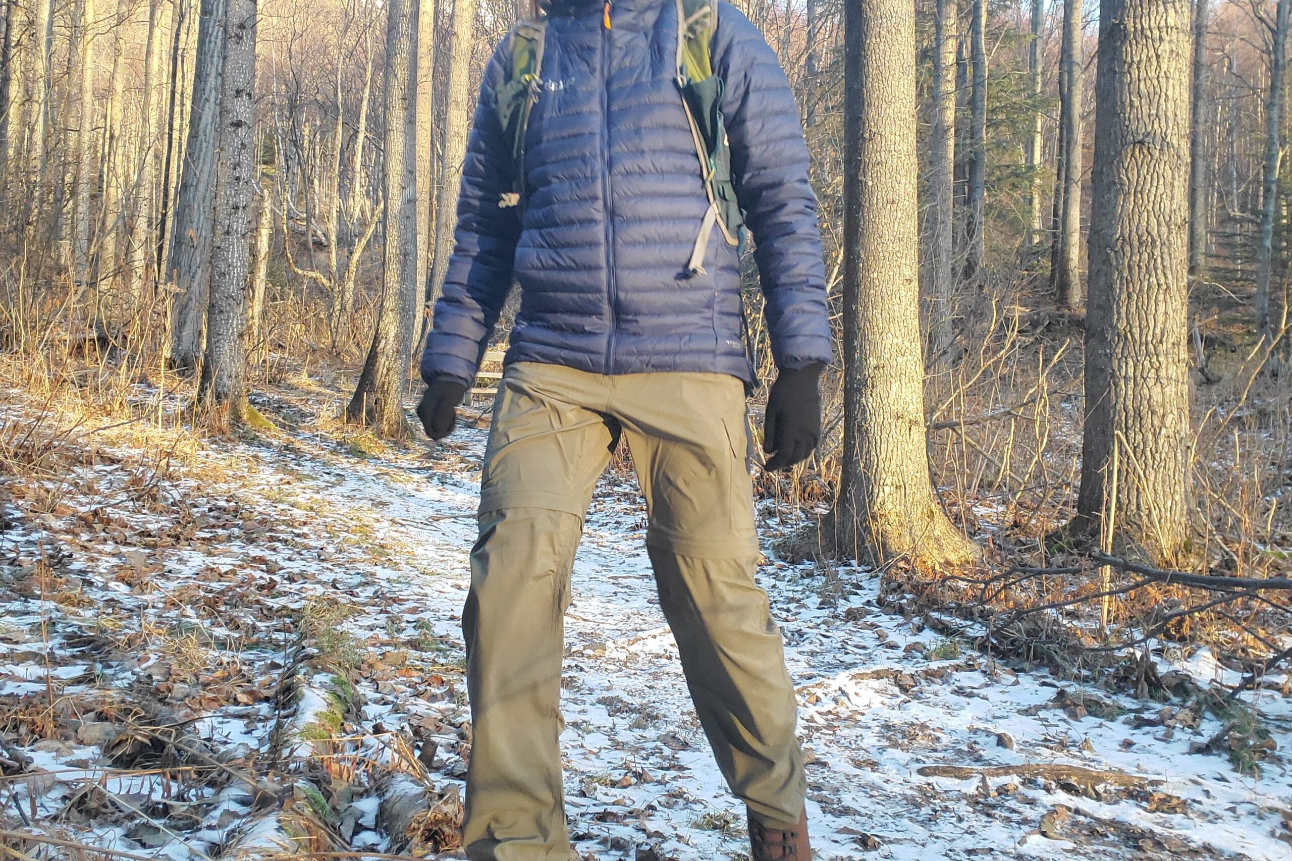 A man walks down a snowy trail in hiking pants.