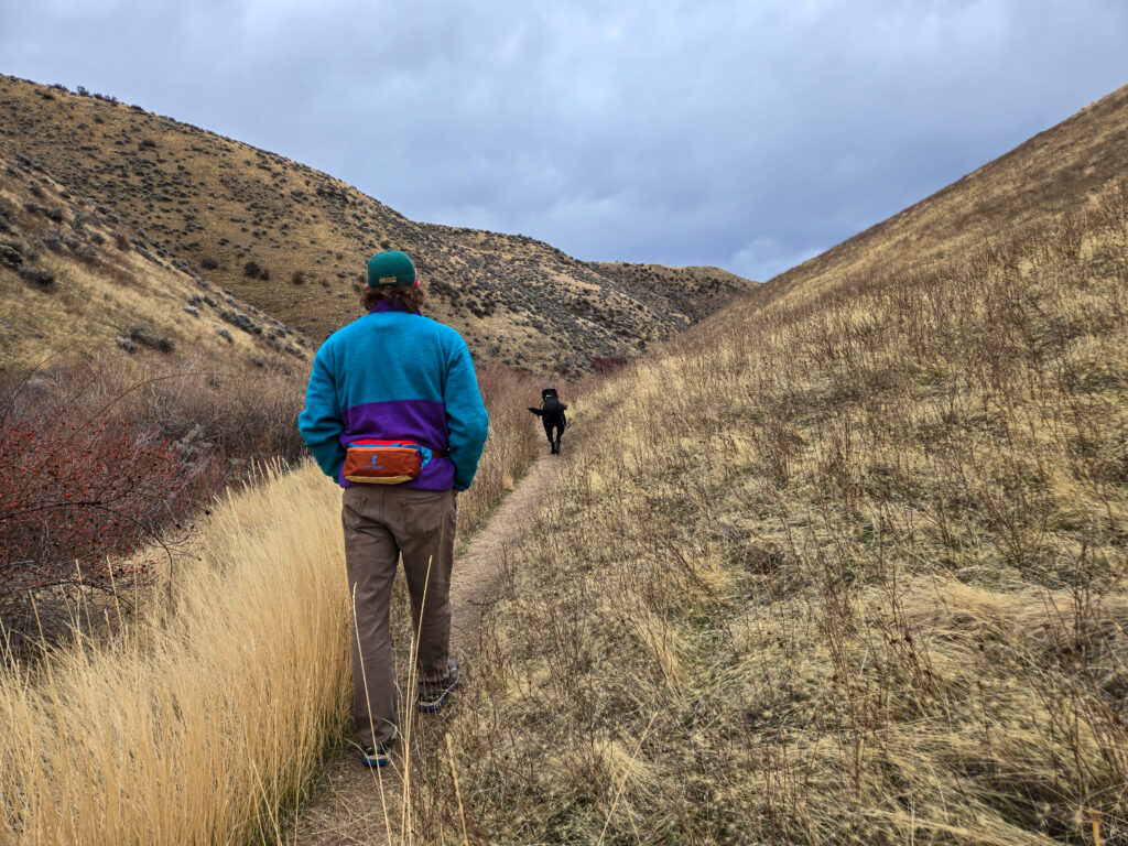 man walking his dog on a desert trail wearing a cotopaxi fanny pack