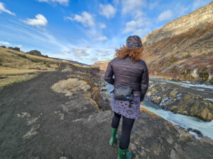 a woman wears a zpack front utility pack accessory on her lumbar walking next to a river in the high desert