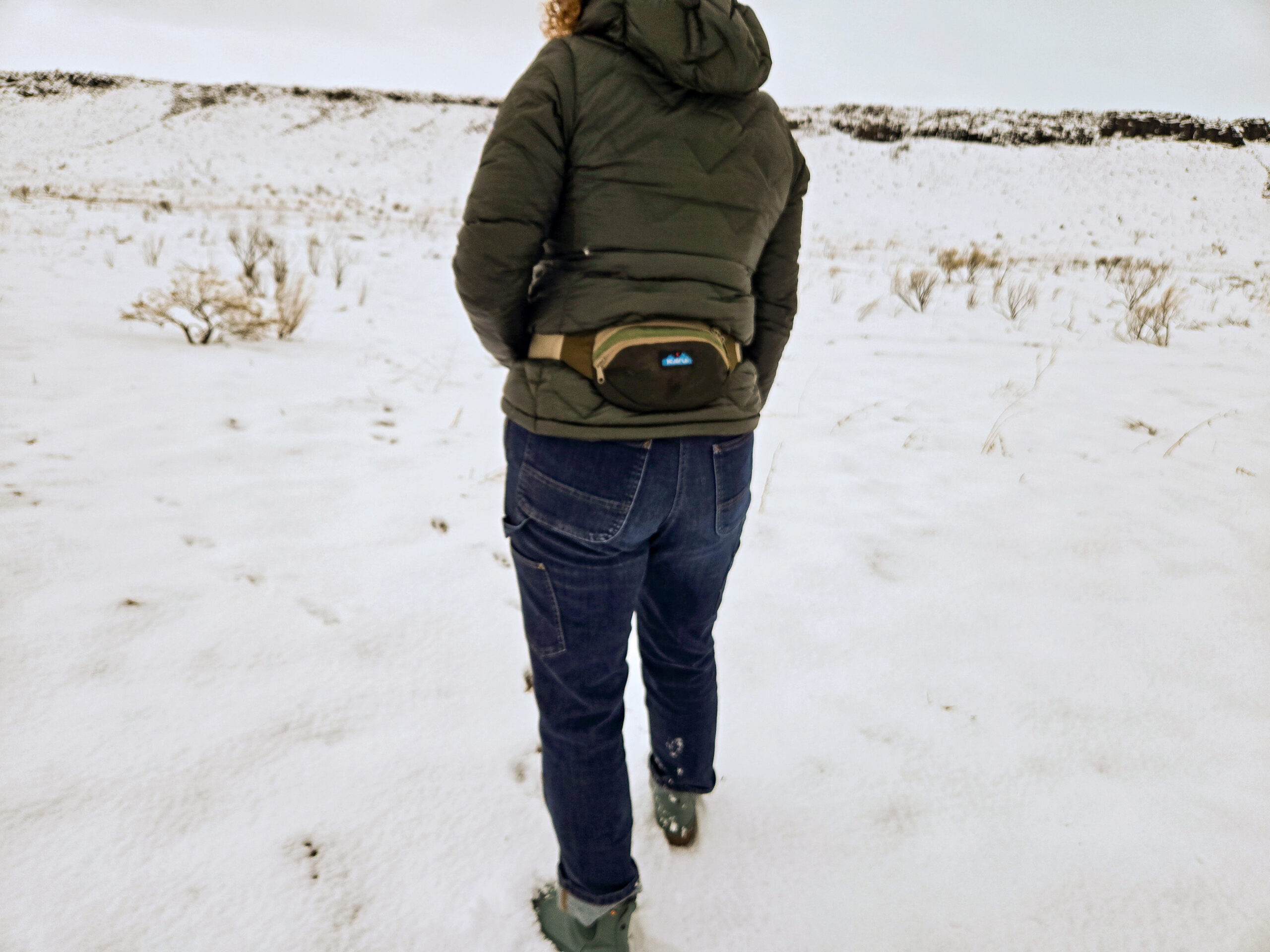 woman walking in snowy field wearing the kavu spectator fanny pack