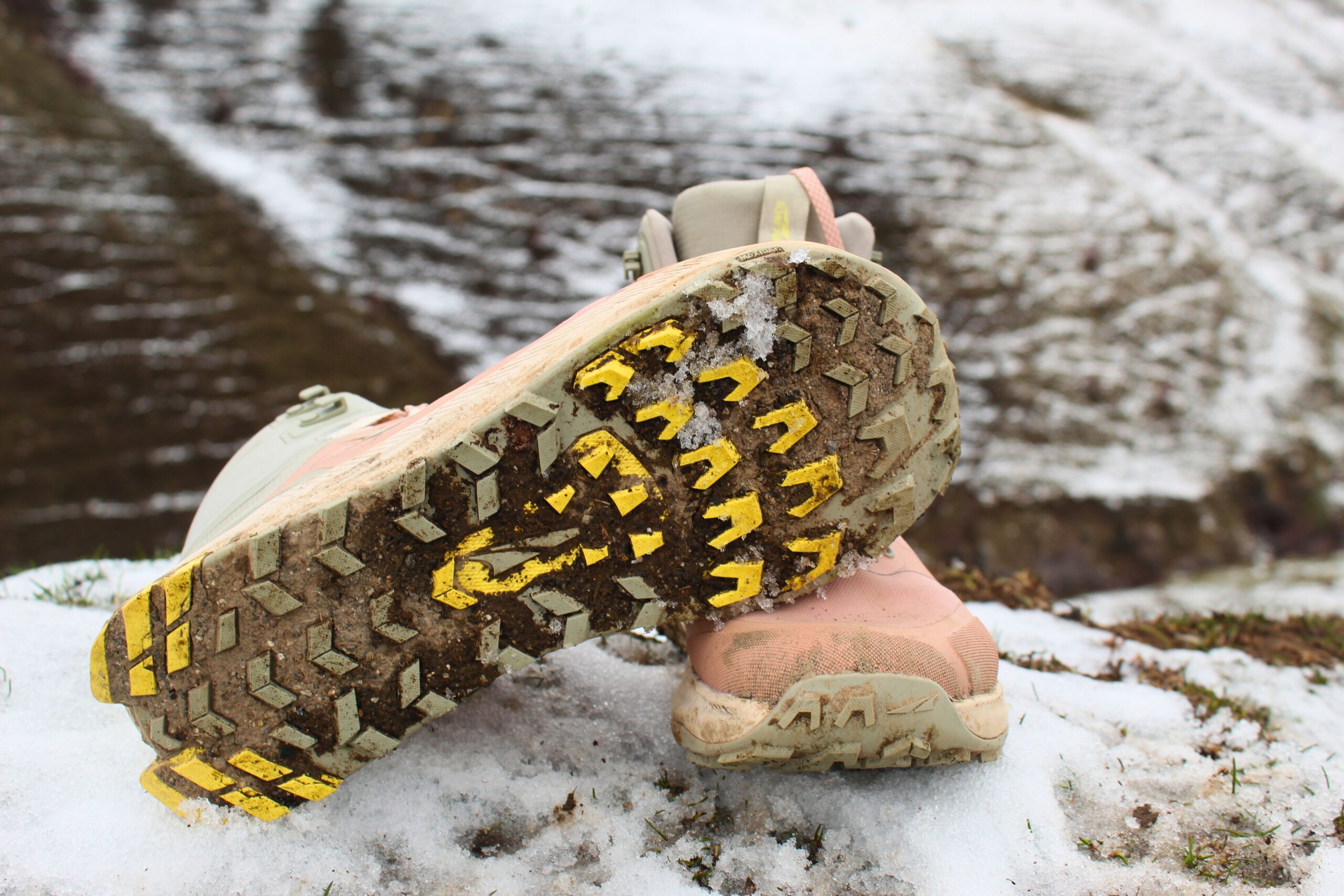 A pair of Women’s Altra Lone Peak ALL-WTHR 2 hiking boots on a snowy hillside showing the sole of one of the shoes