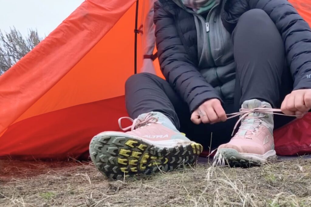 Hiker sitting at the entrance of a tent tying the Women’s Altra Lone Peak ALL-WTHR 2