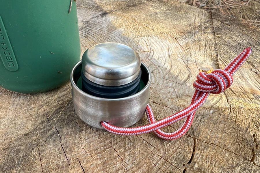 Black+Blum water bottle lid with a red strap resting on a wooden surface.