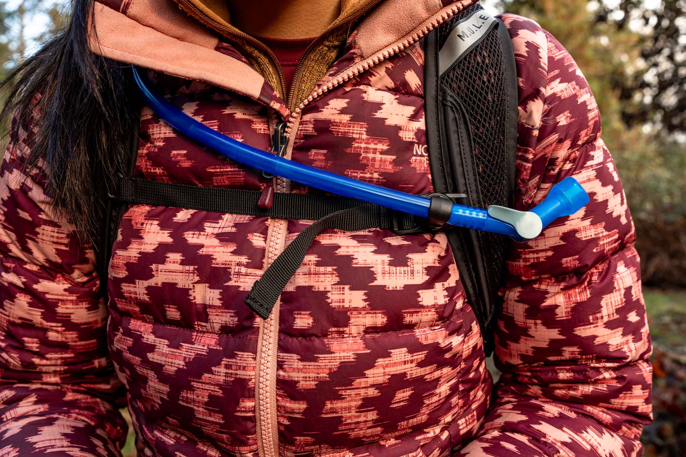 Details of M.U.L.E.® 12 Hydration Pack 100 oz - Close up view of a person wearing the pack and showing the nozzle of the hydration bladder and attachment