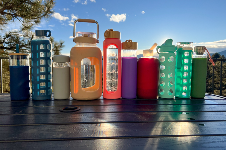 A variety of reusable water bottles arranged on a table with a scenic mountain sunset in the background, showcasing different shapes, colors, and designs.