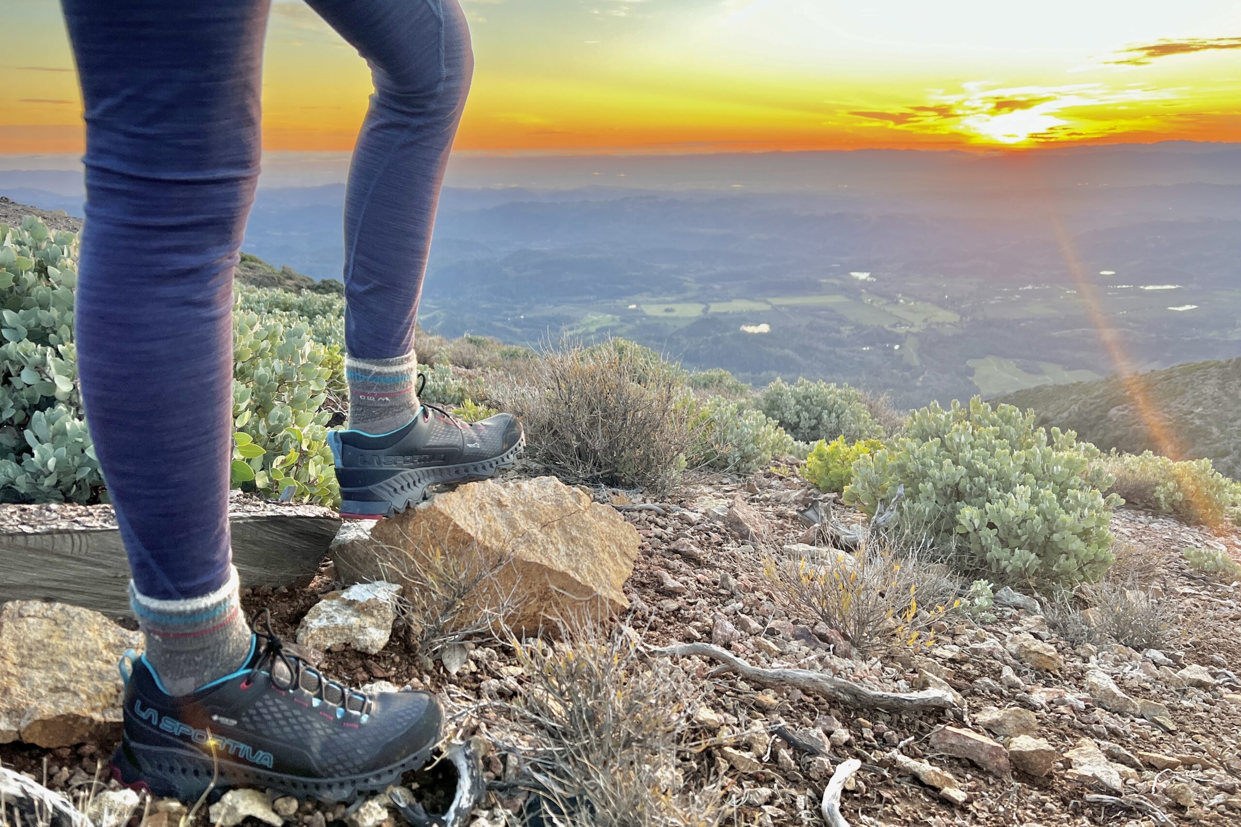 Close-up showing the La Sportiva shoes in varied terrain with rocks, bushes and sticks.