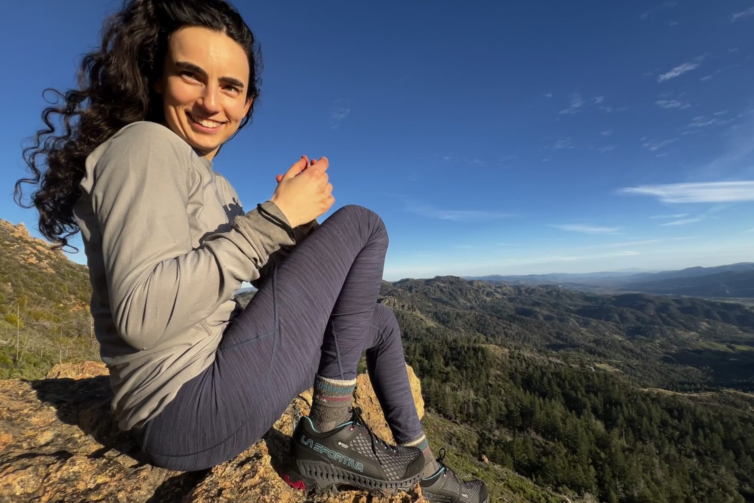 A woman sits on a rocky ledge wearing La Sportiva shoes.