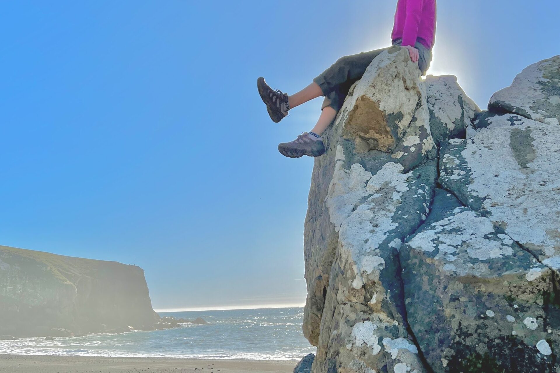 Women sitting on top of a large boulder with the beach in the background.