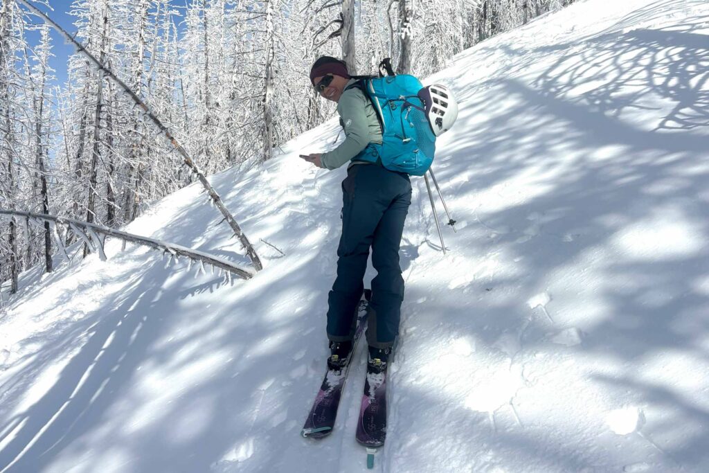 Gregory Juno 24 H2O pack used by a person on skis against a snowy hill with snowy trees on a sunny day