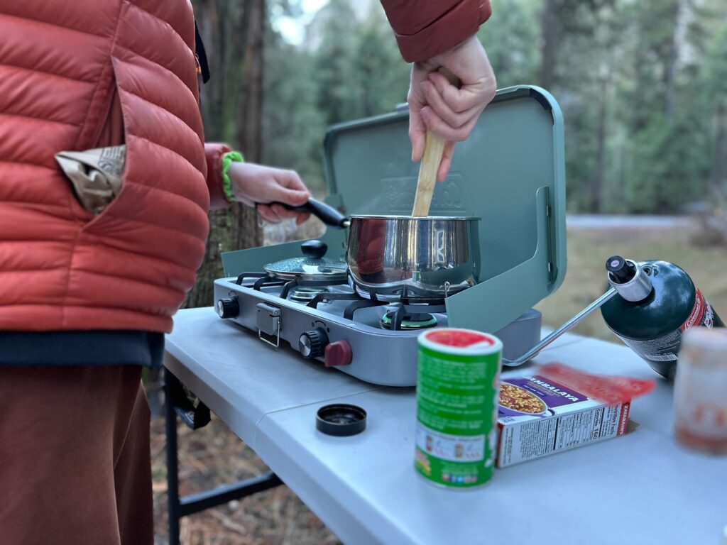 Blue camp stove at forested camp site making rice, burritos, and breakfast.