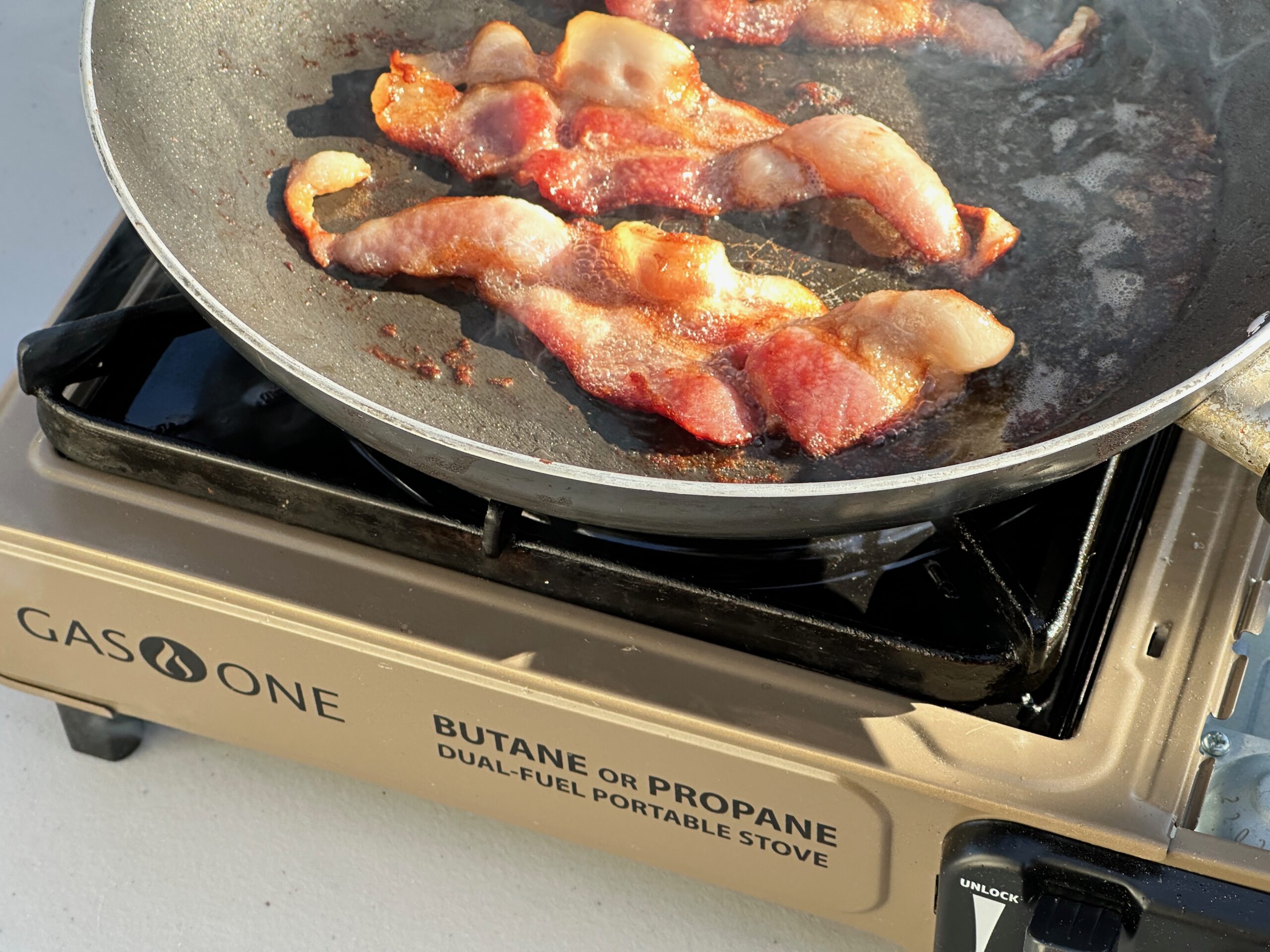 the Gas ONE GS-1000 cooking bacon at camp, showing off how evenly it can cook. 