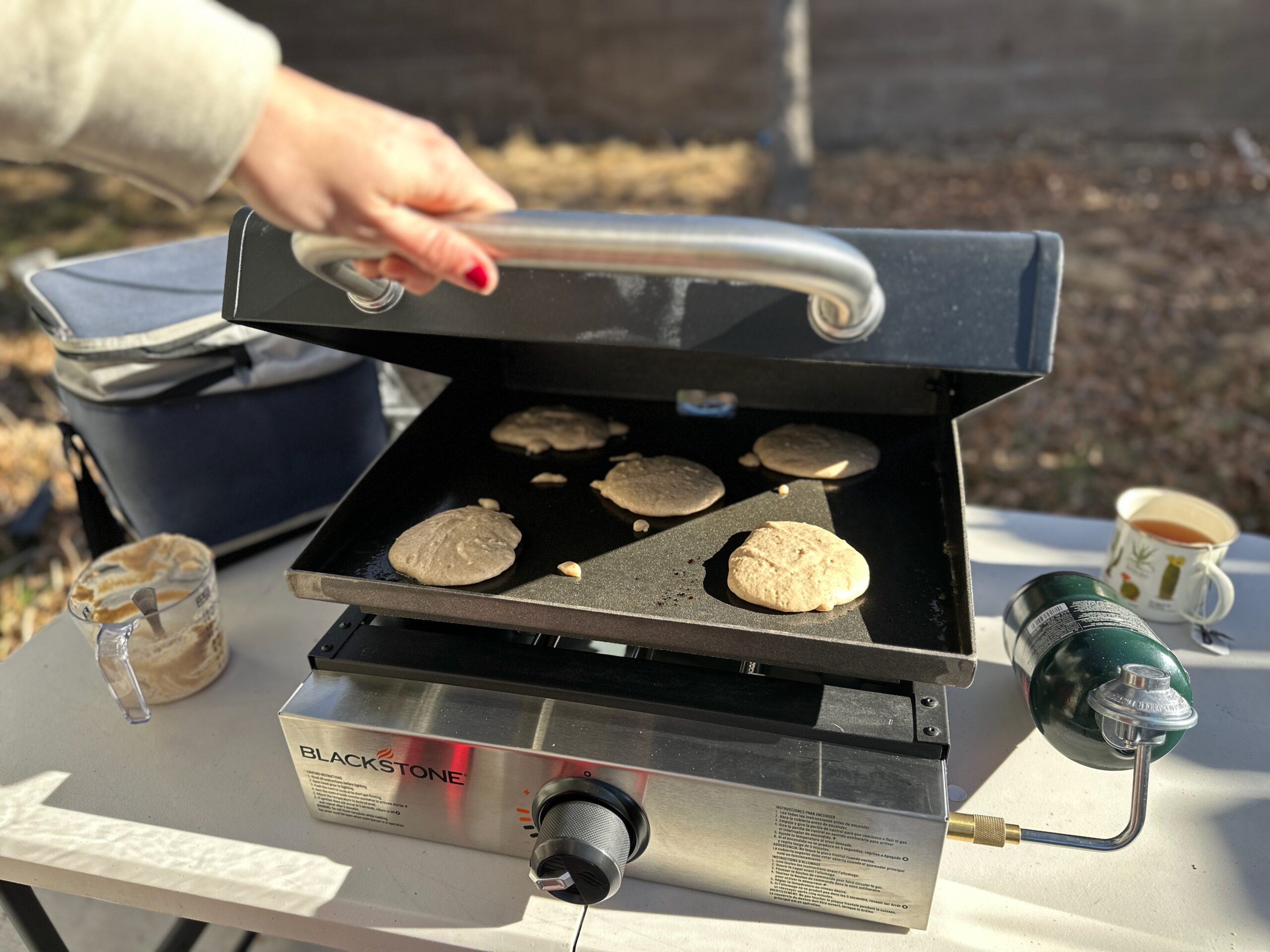 a woman opening the Blackstone Original 17" Tabletop Griddle with Hood with the easy-to-use handle