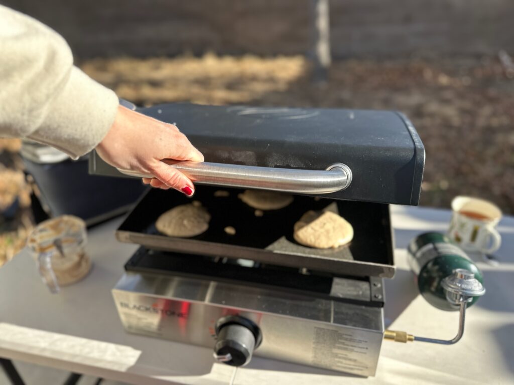 a woman opening the Blackstone Original 17" Tabletop Griddle with Hood with the easy-to-use handle