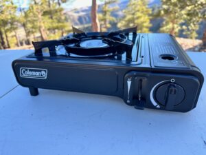 The Coleman Classic 1-Burner Butane Camping Stove cooking various meals at a campsite within the pines