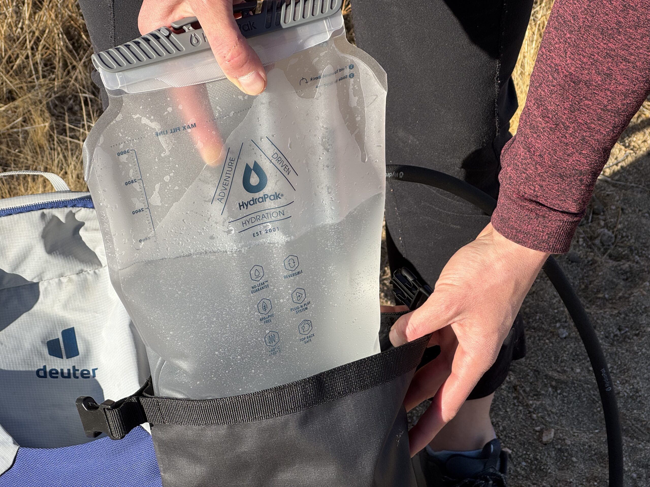 Close up of a hiker sliding a non insulated hydration bladder into an insulated sleeve.