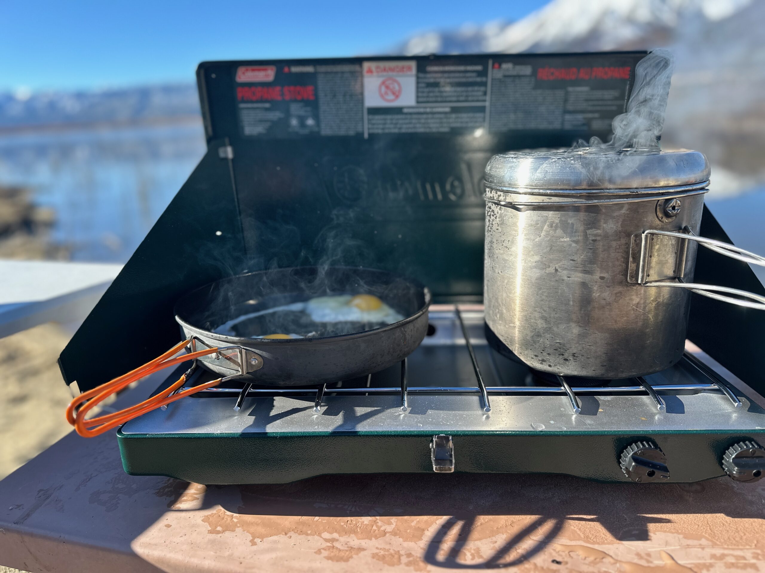 the Coleman Cascade Classic 2-Burner cooking camp meals at a beachside camp