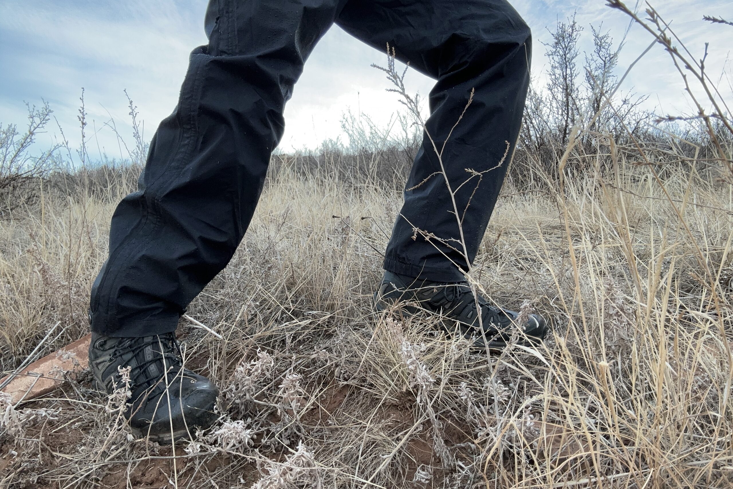 Closeup of someone wearing the black Patagonia Torrentshell rain pants, walking on a trail.