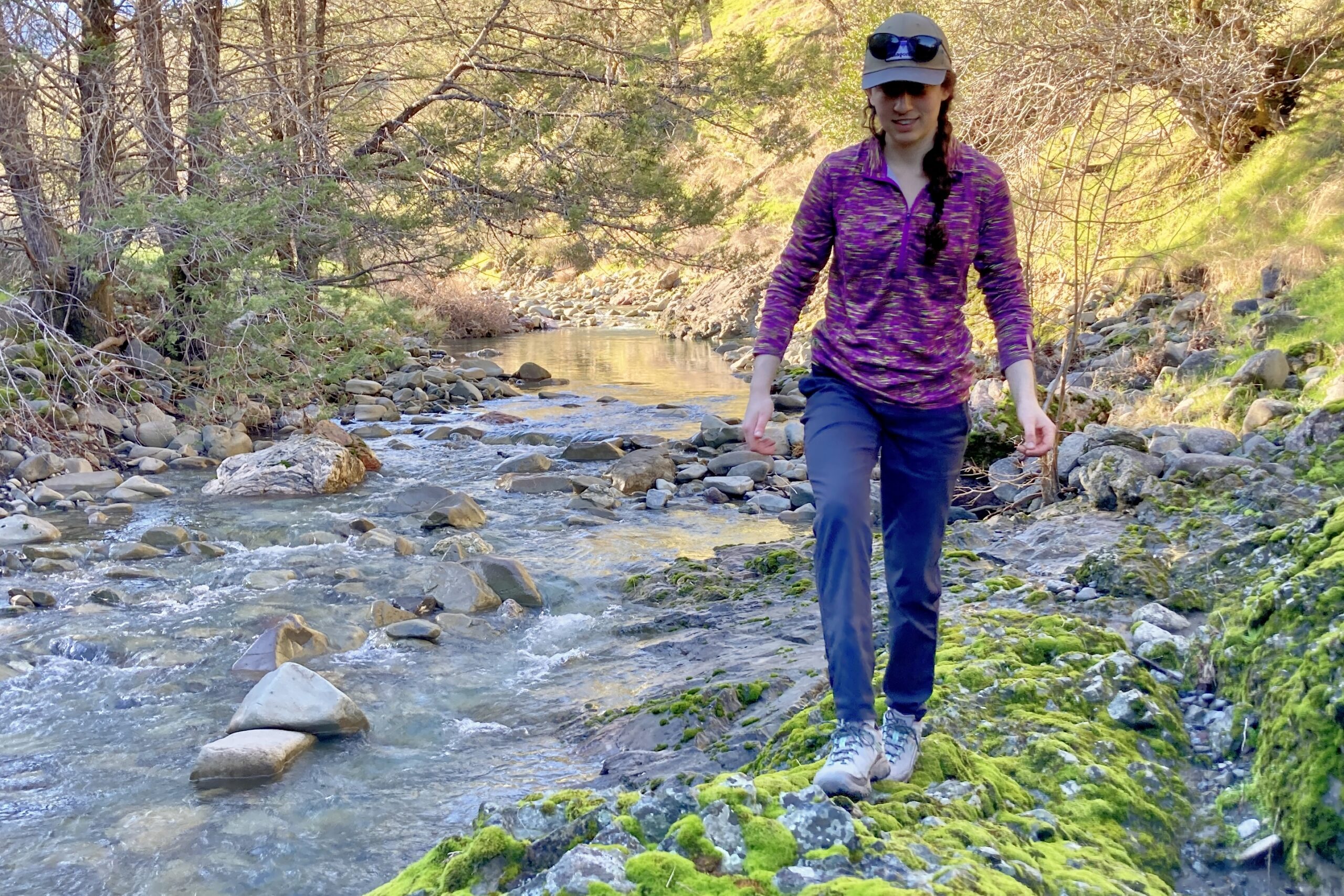 Women walking across a mossy rock along a creek.