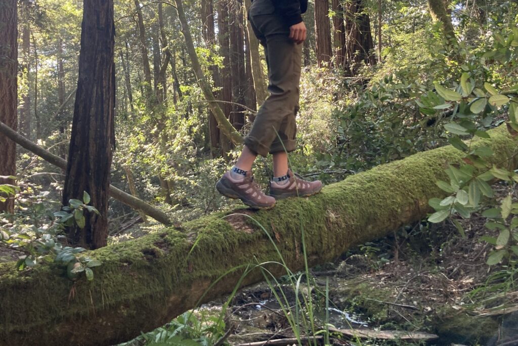 Women standing on a mossy log wearing Oboz hiking shoes.