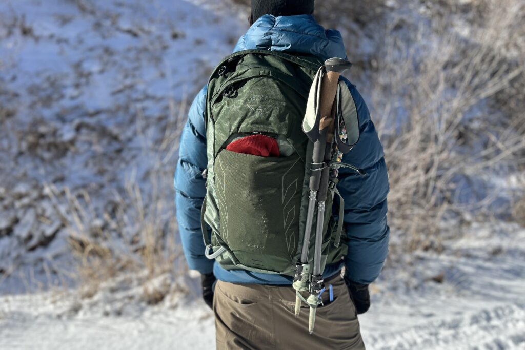 A person wears a backpack facing away from the camera in a snowy setting.