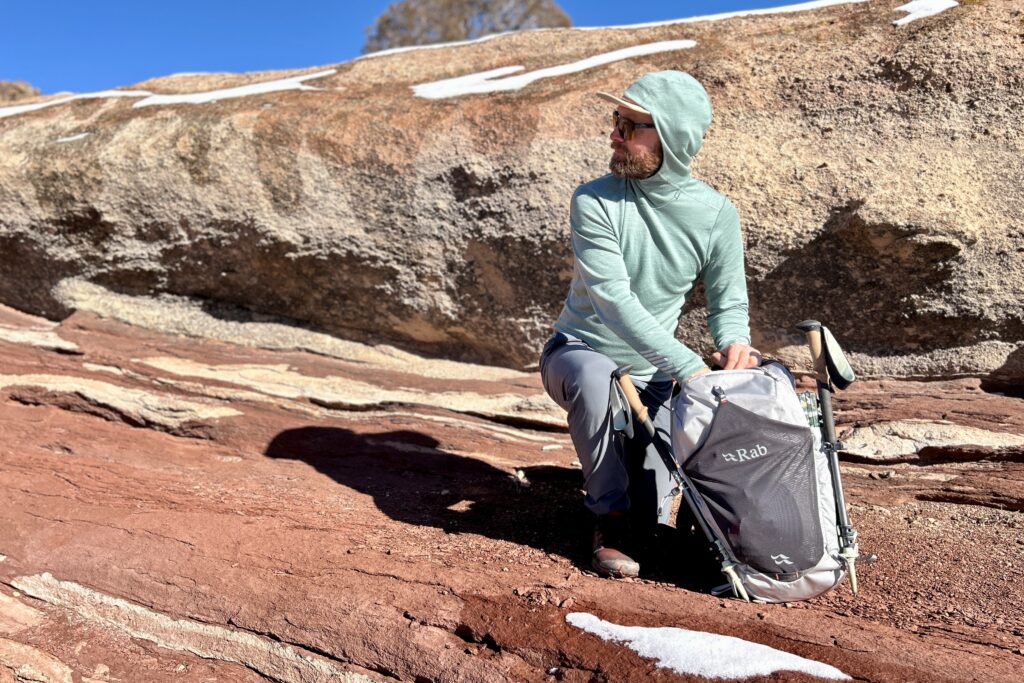 A man looks off in the distance as he bends over and digs through his backpac.