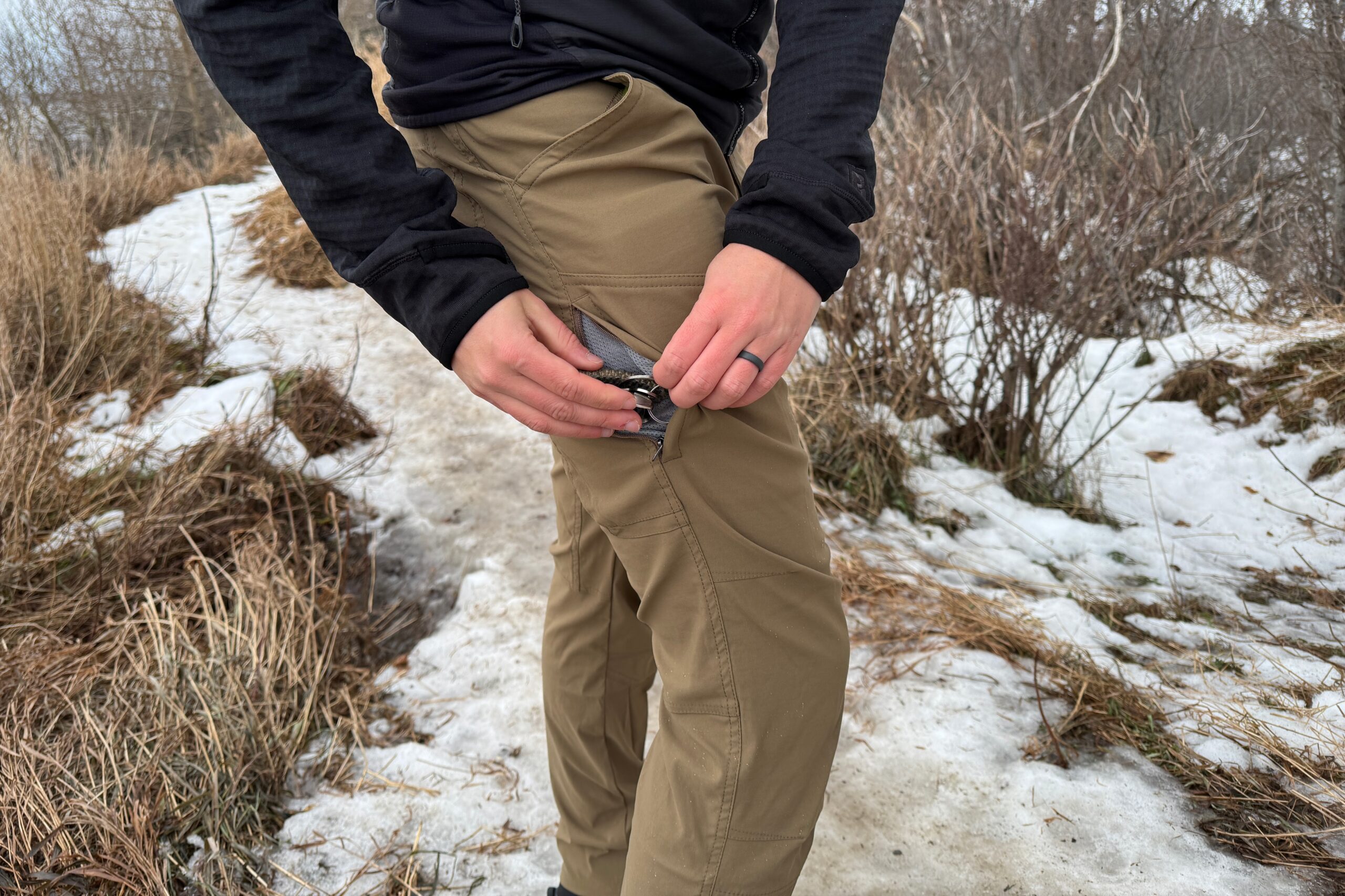 A man puts car keys in the side pocket of his hiking pants.