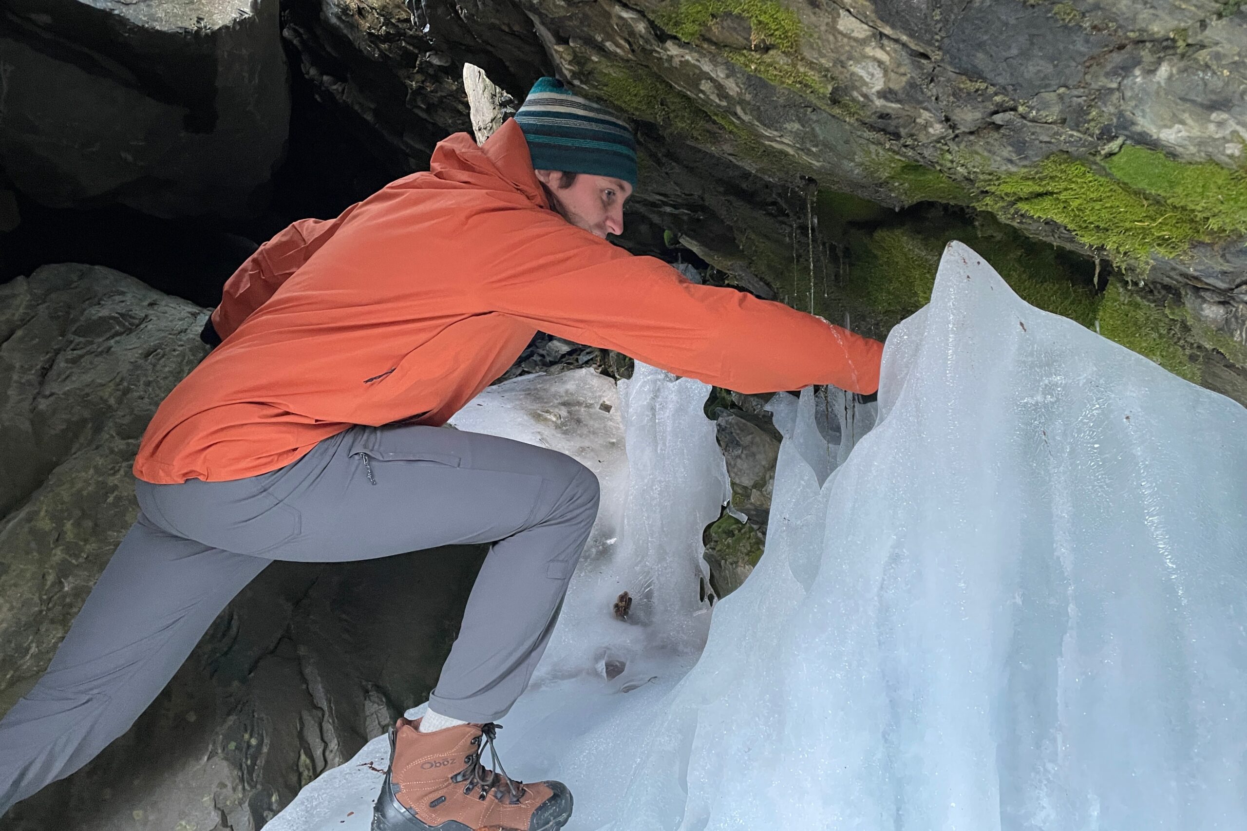 A man leans into an ice cave.