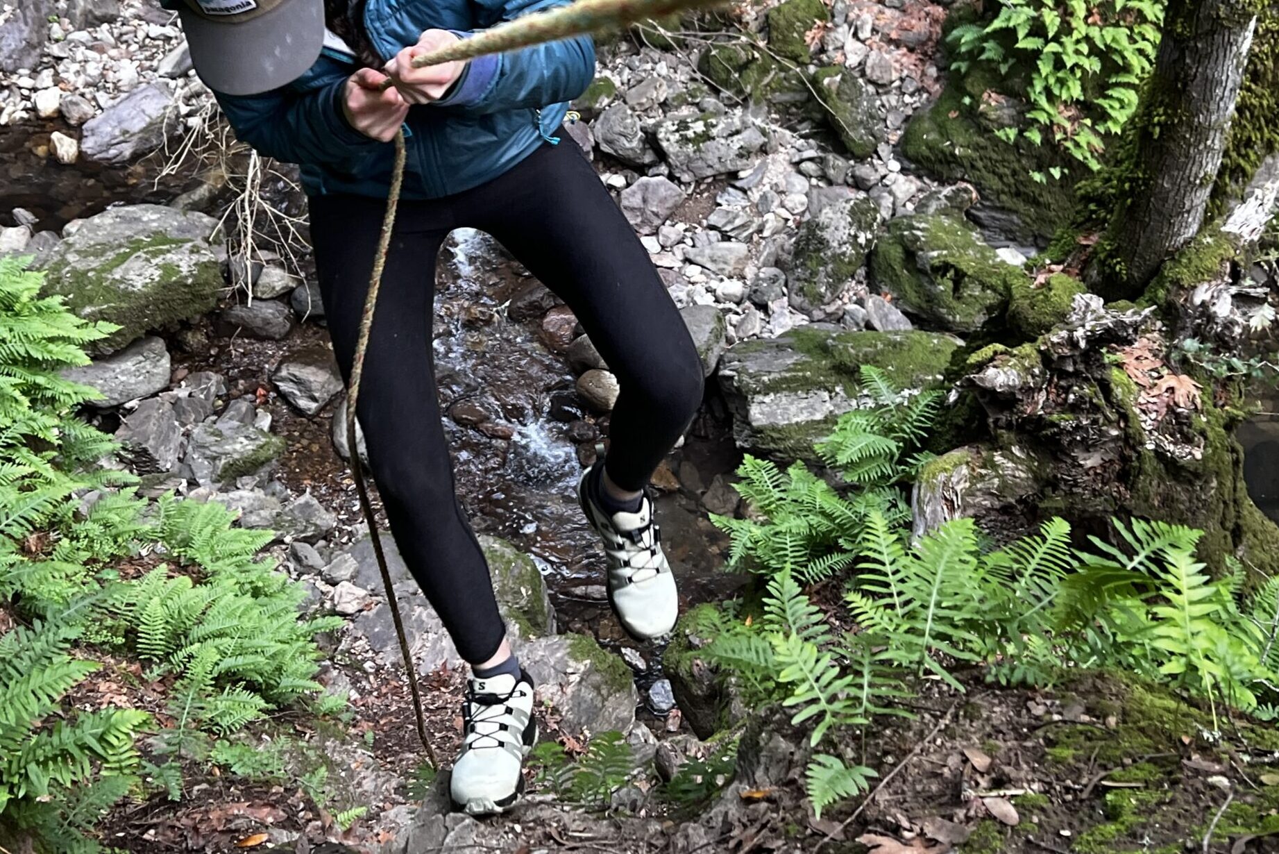 Women holding a rope as she descends down a steep trail with a creek far below in the background.