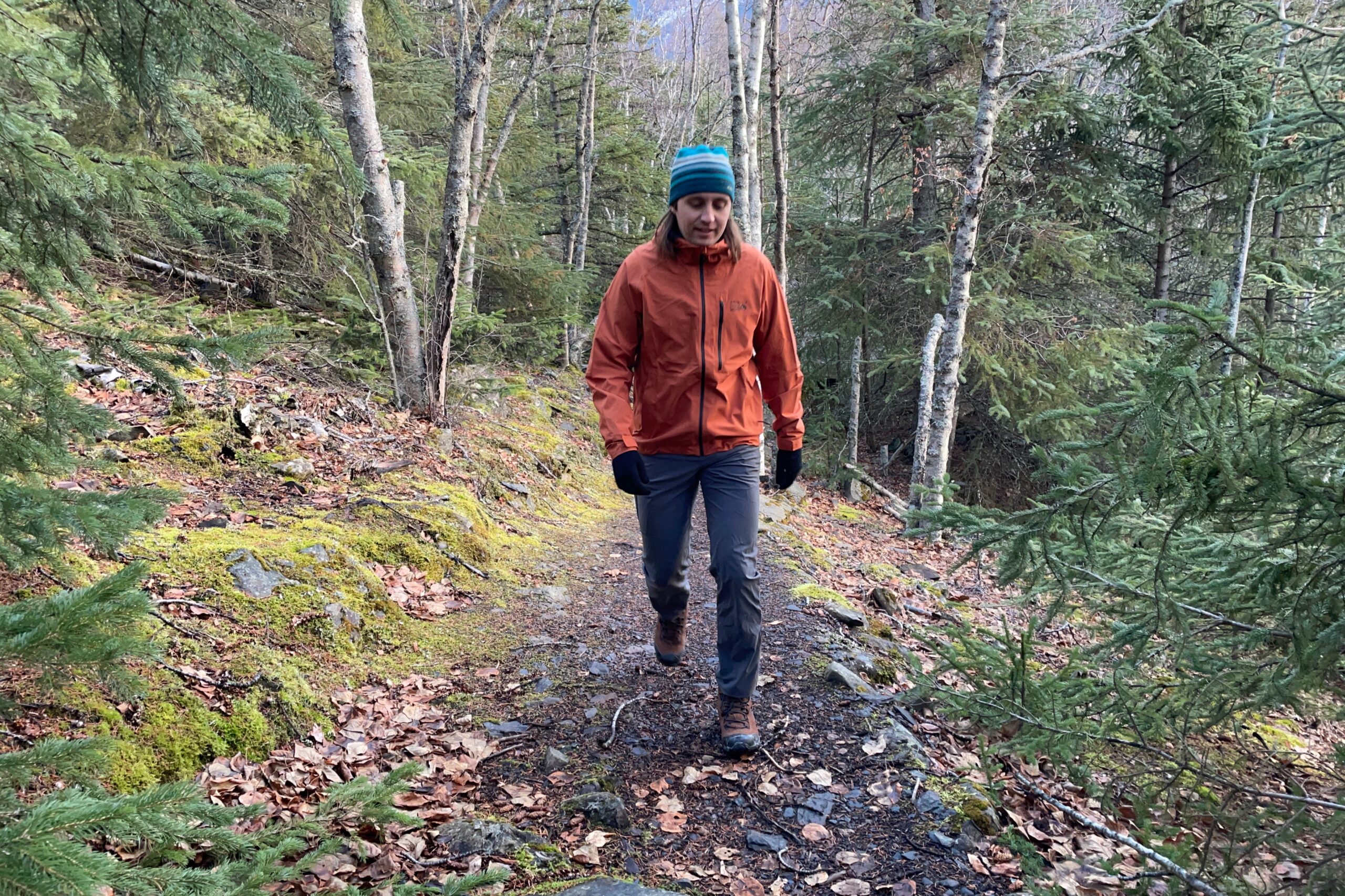 A man walks up a hill on a trail in early winter.