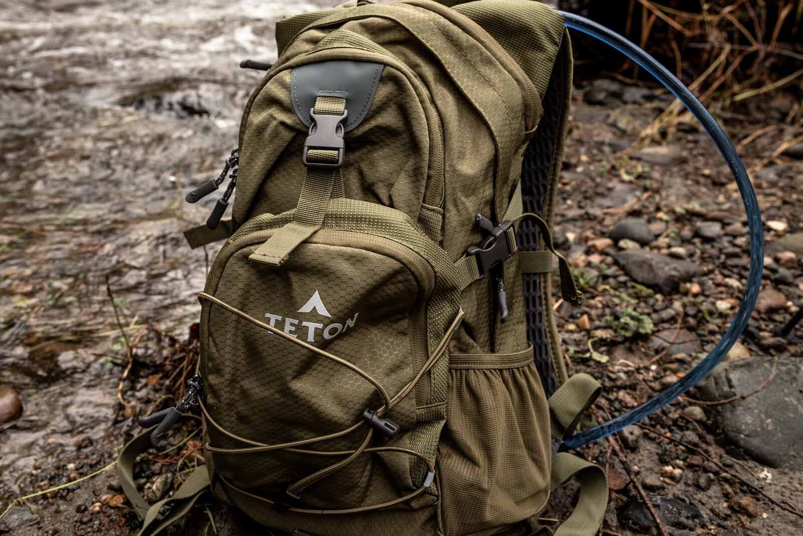 Details of TETON Sports Oasis 18L Hydration Pack - the pack is sitting on the ground by a river