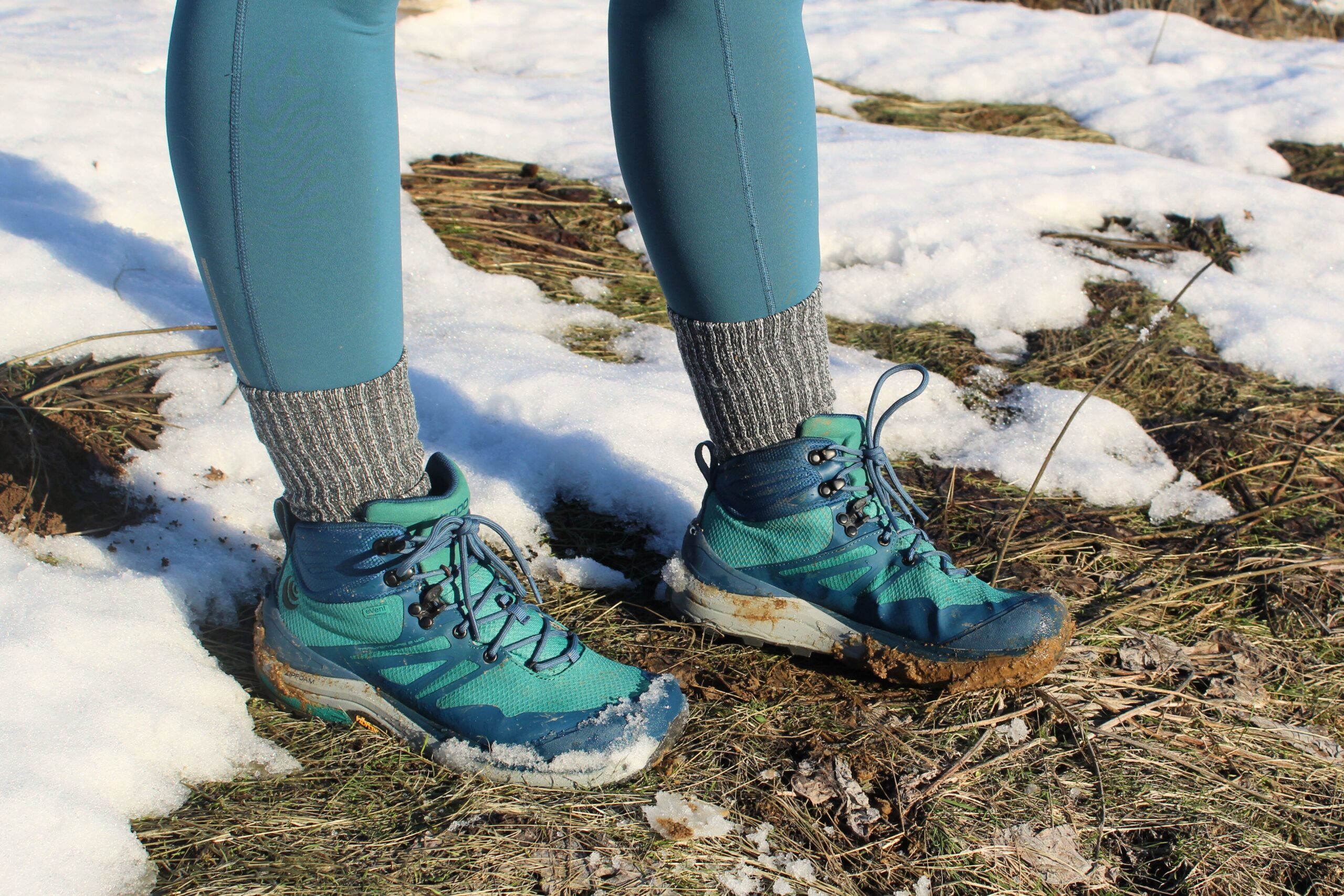 Hiker standing in grass and snow wearing the Women’s Topo Trailventure 2 WP