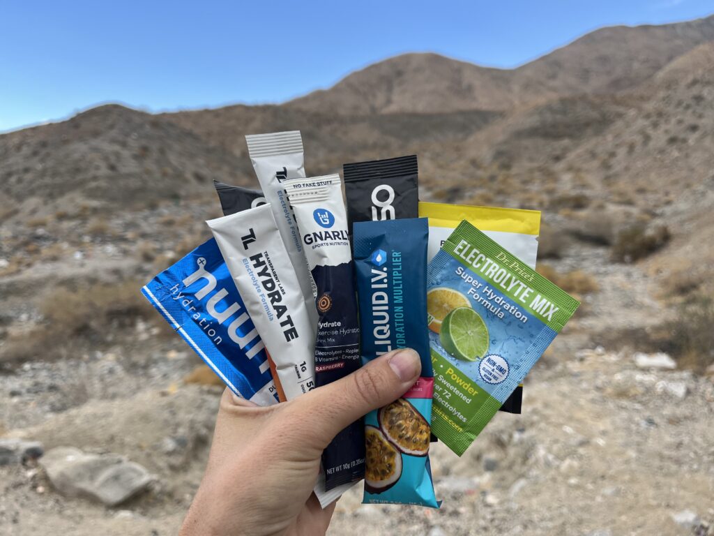 A hand holding up several electrolyte single-serve packets from different brands