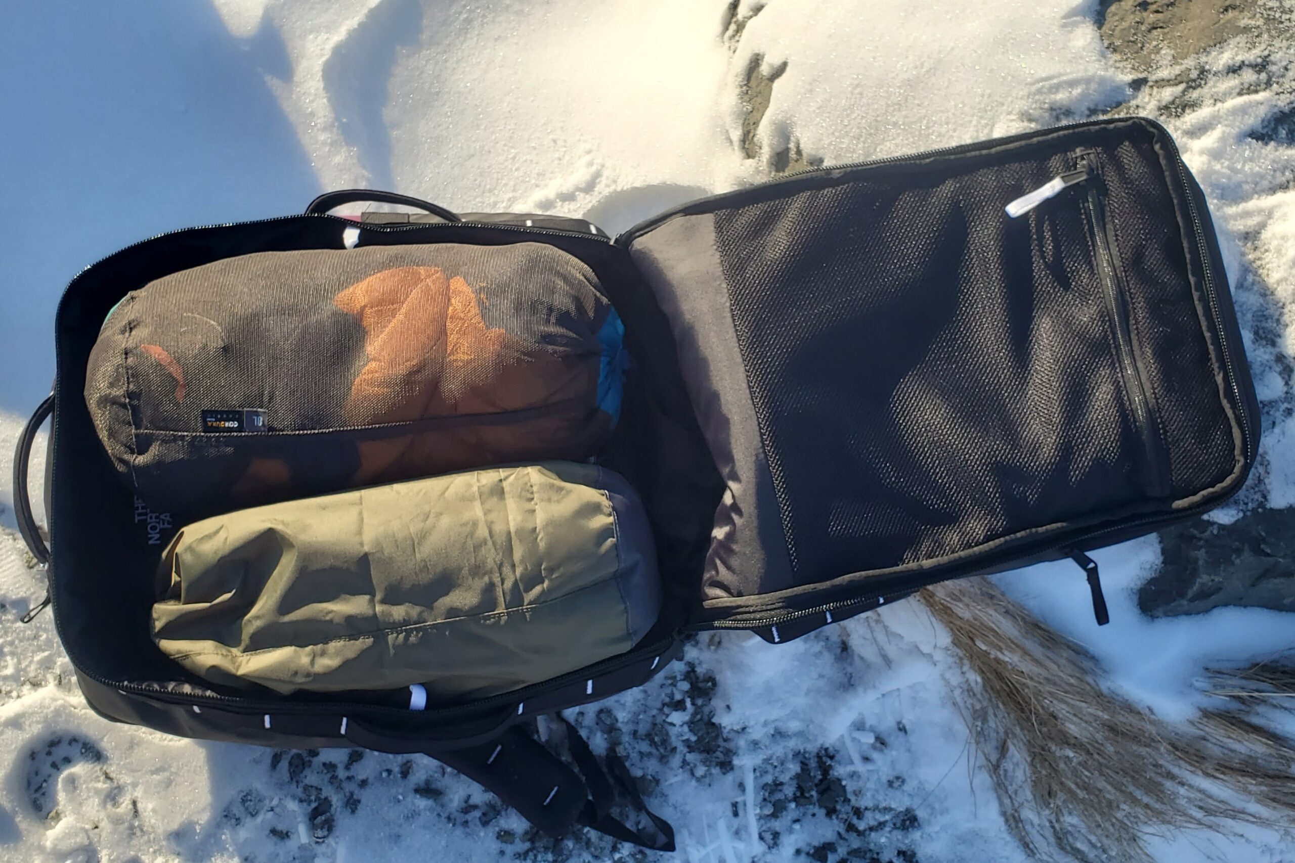 A backpack sits on a snowy path fully unzipped.